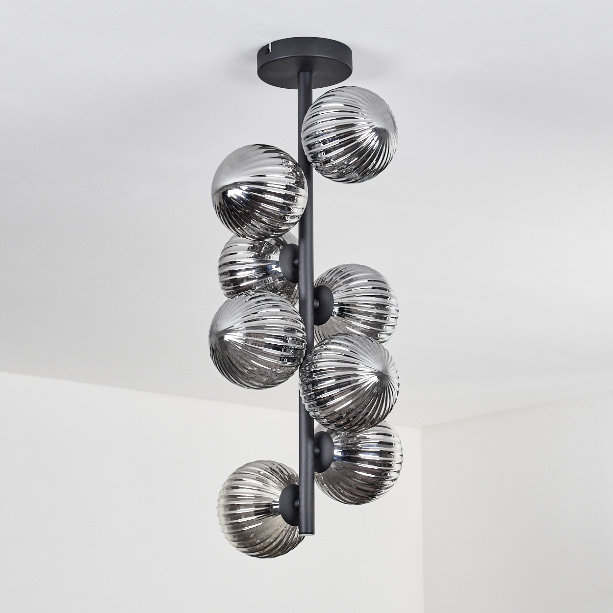 Eine schwarze Deckenlampe mit neun silbernen, gerippten Glaskugeln, die in einem weißen Raum hängen.