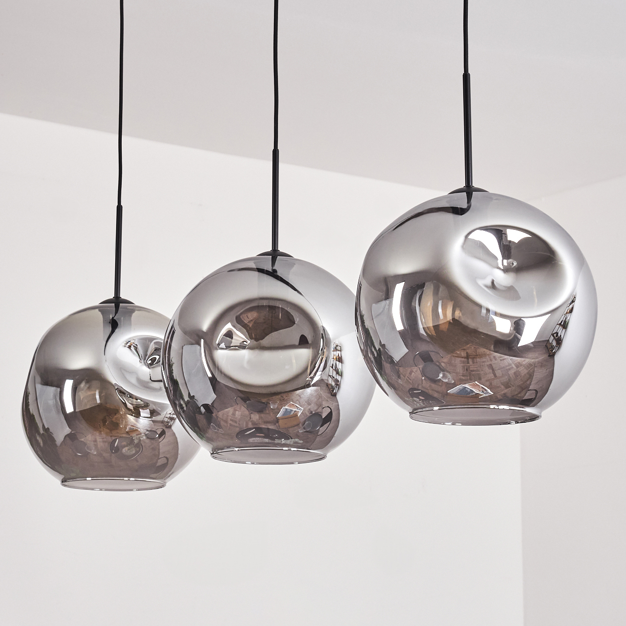 Drei silberne Kugelleuchten, die von einer weißen Decke hängen, jede mit einem schwarzen Kabel. Die Kugeln reflektieren den Raum.