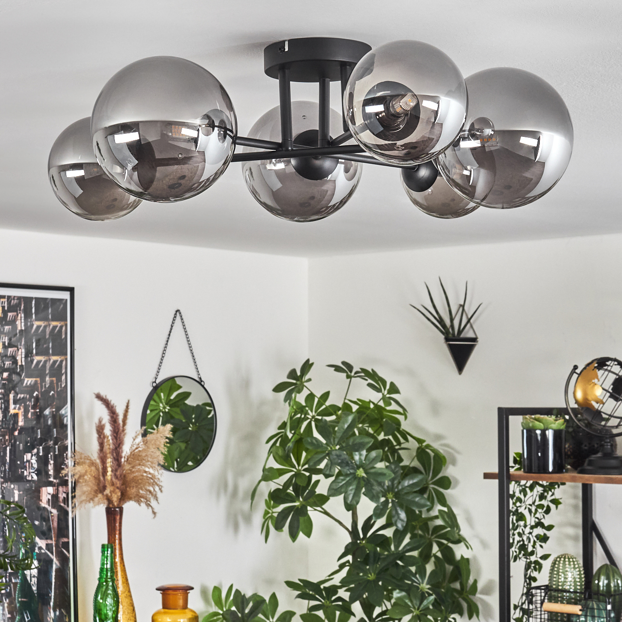 Eine Deckenlampe mit sechs Kugeln, einem Spiegel und Pflanzen. Der Hintergrund umfasst Regale mit Dekoration.