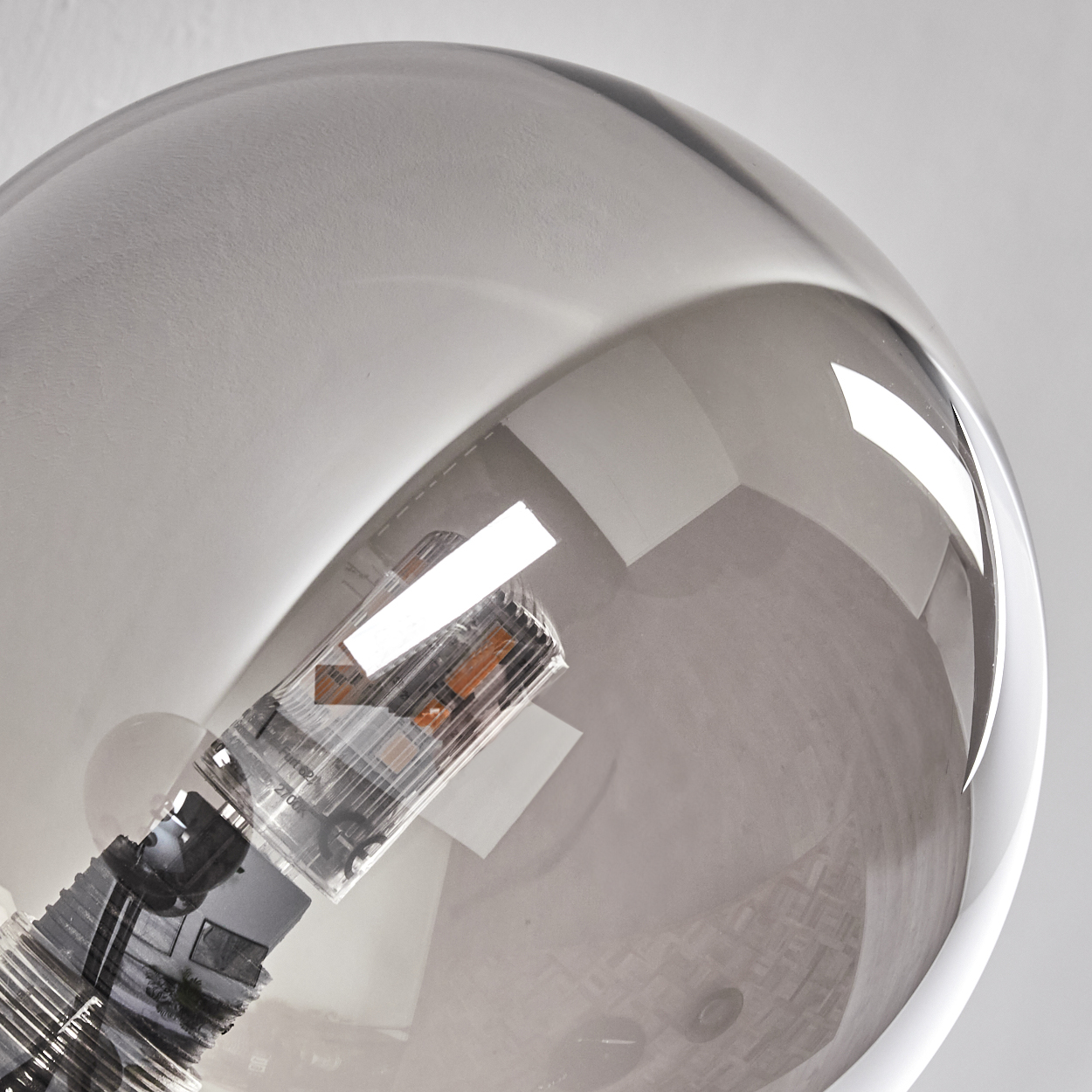 Nahaufnahme einer Glaskugel mit einer Glühbirne im Inneren. Das Glas reflektiert einen Raum mit weißen Wänden.