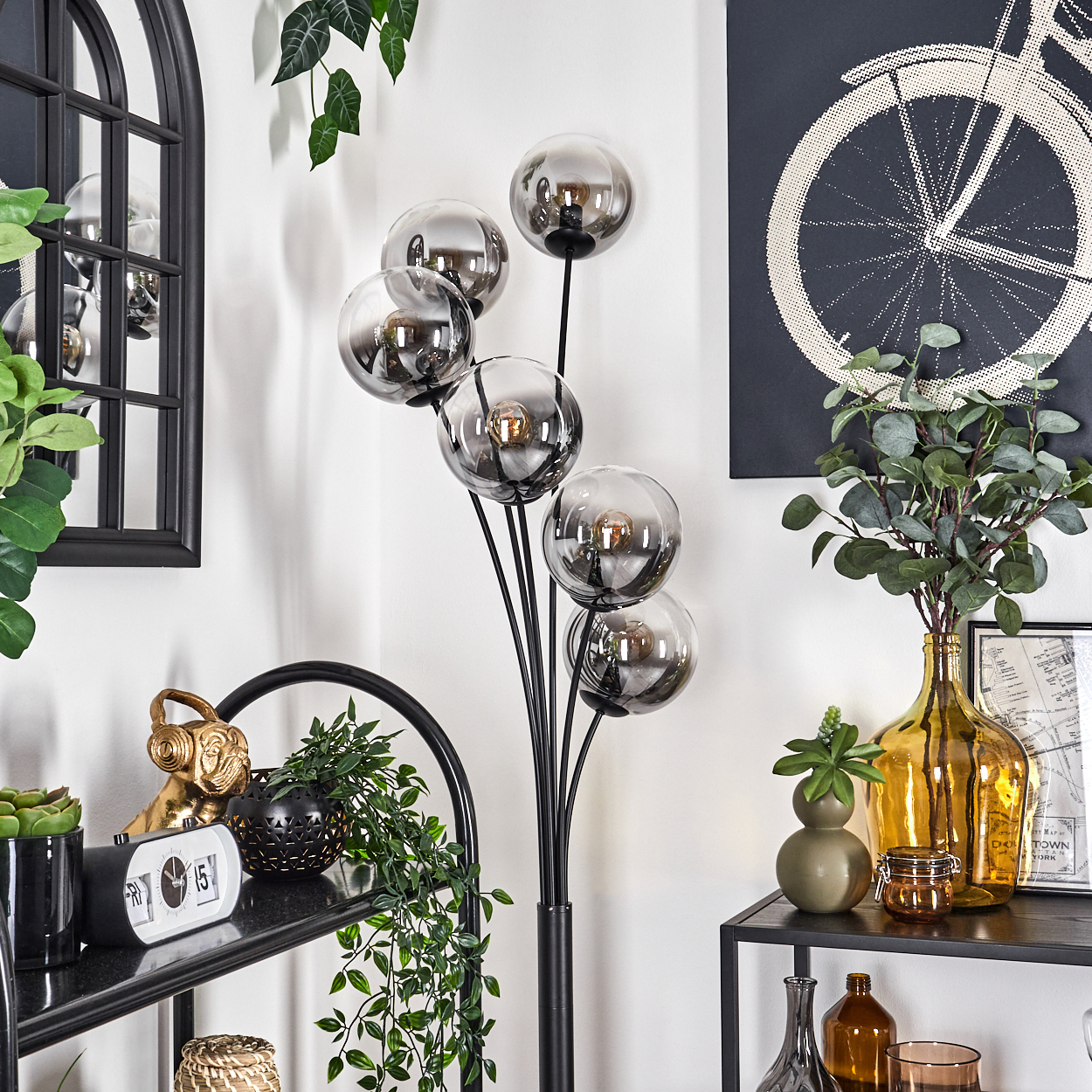 Stehlampe mit silbernen Kugeln, schwarzem Stiel und Zimmer mit Deko. Spiegel, Pflanzen und Kunstwerk vorhanden.