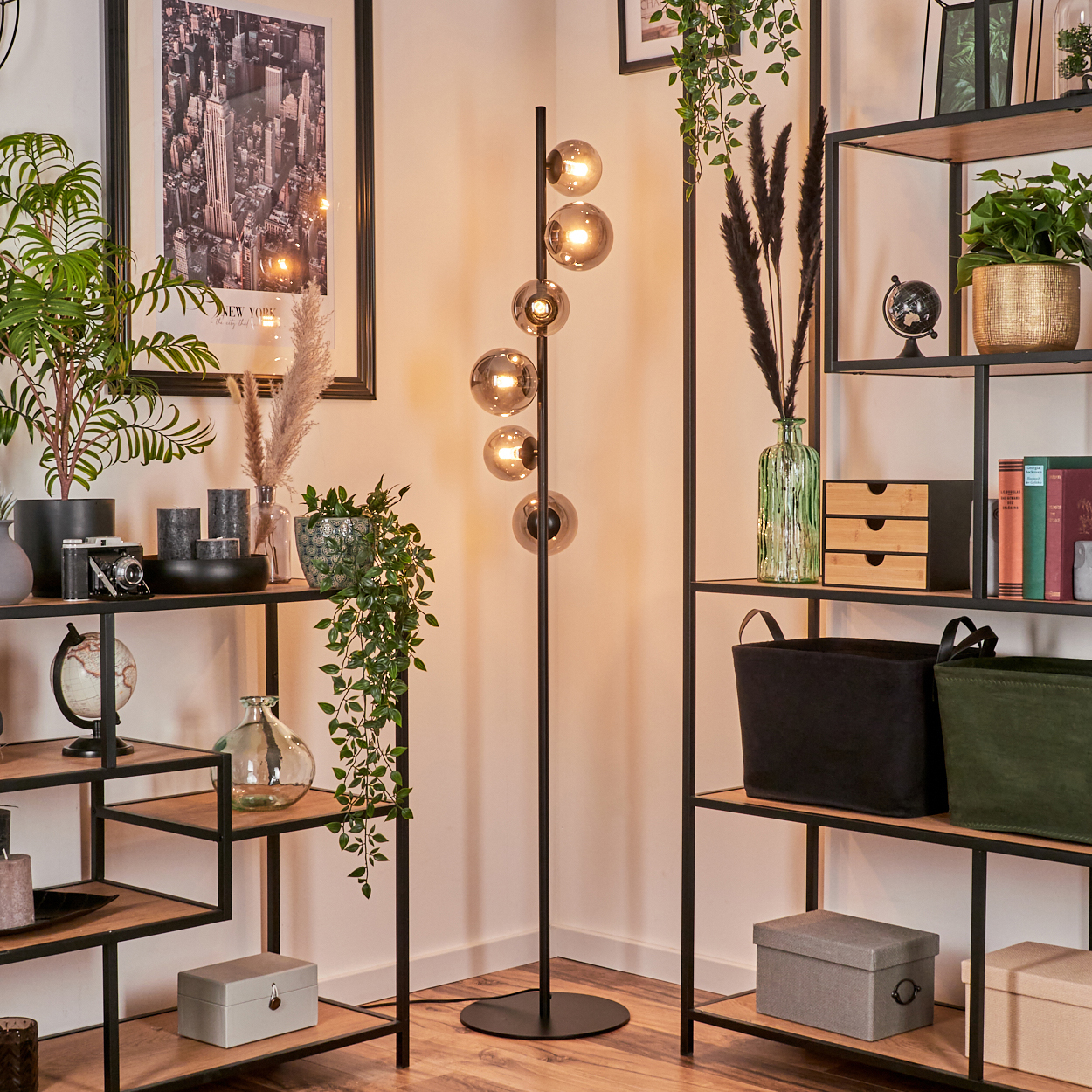 Eine schwarze Stehlampe mit sechs Glaskugeln in einem Raum mit Regalen, Pflanzen und Kunstwerken.