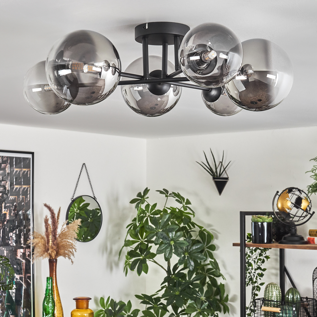 Eine schwarze Deckenlampe mit Glaskugeln, mit einem Raum im Hintergrund mit Pflanzen und Dekoration.