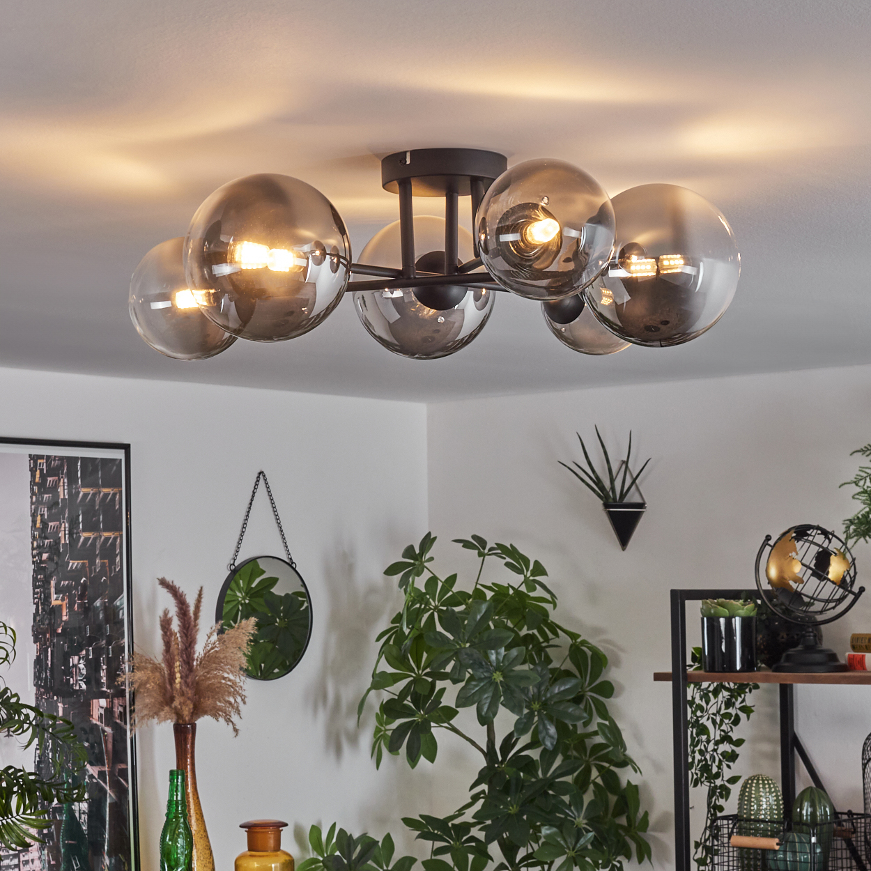 Eine Deckenleuchte mit Glaskugeln beleuchtet einen Raum mit Pflanzen und Kunstwerken.