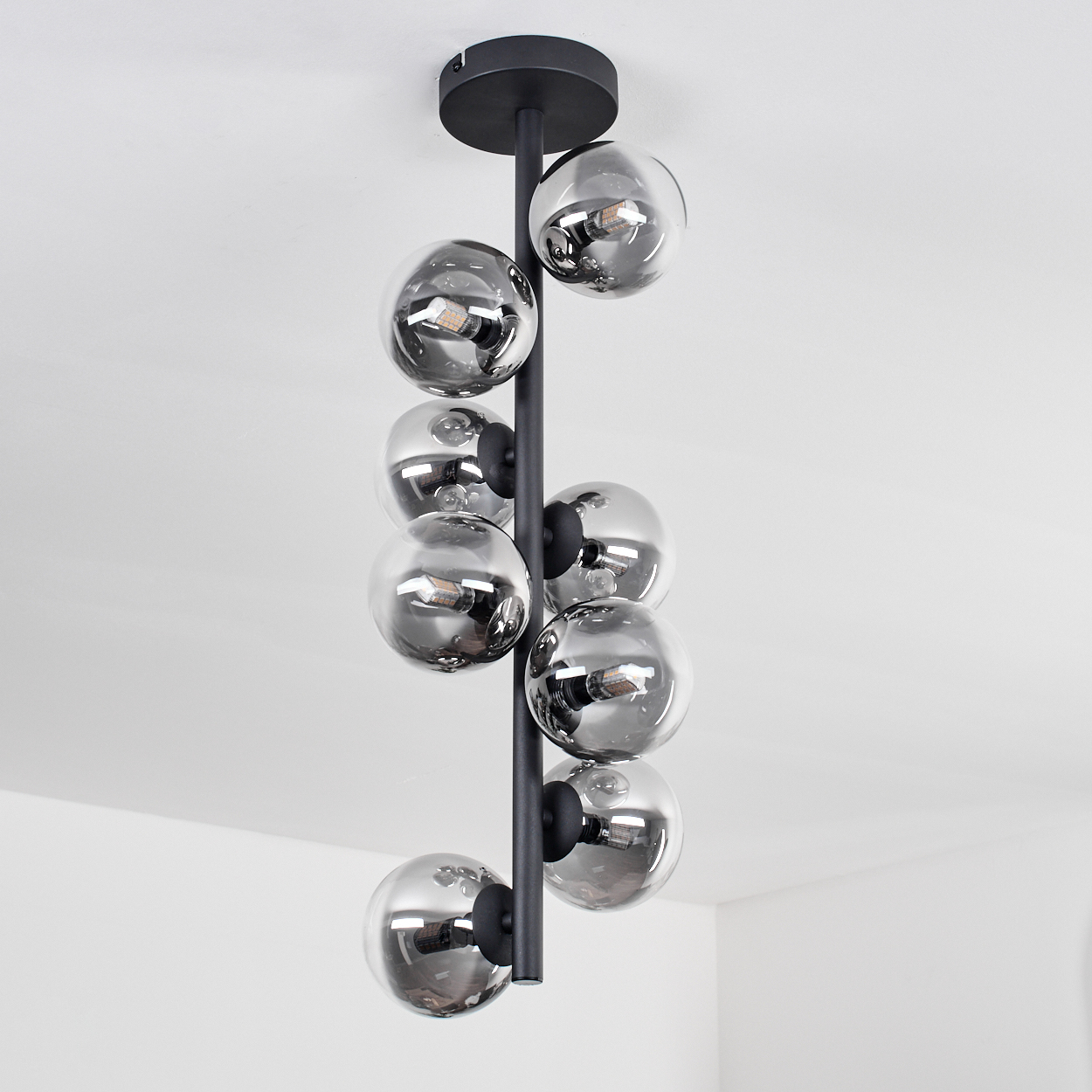 Eine schwarze Pendel-Deckenleuchte mit neun Glaskugelschirmen, beleuchtet vor einer weißen Decke.