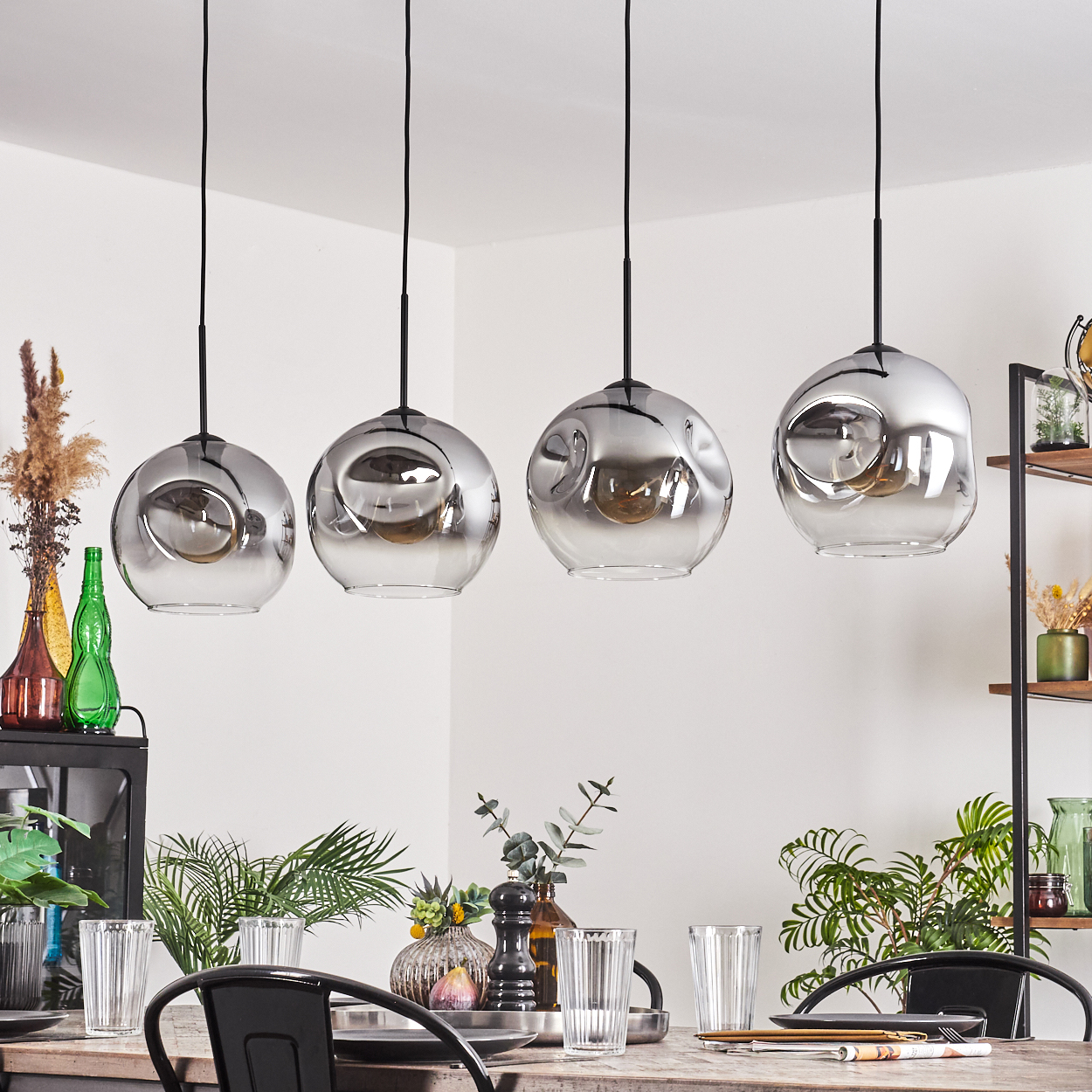 Vier Hängelampen hängen vor einer weißen Wand. Die Lampen sind kugelförmig.