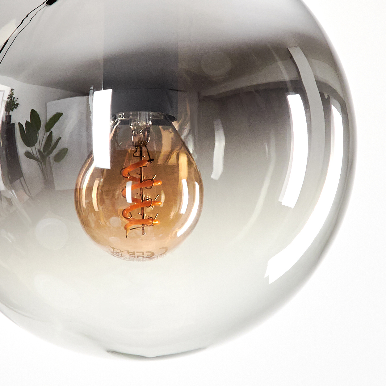Nahaufnahme einer transparenten Glaskugel mit einer Glühbirne im Inneren, vor weißem Hintergrund.