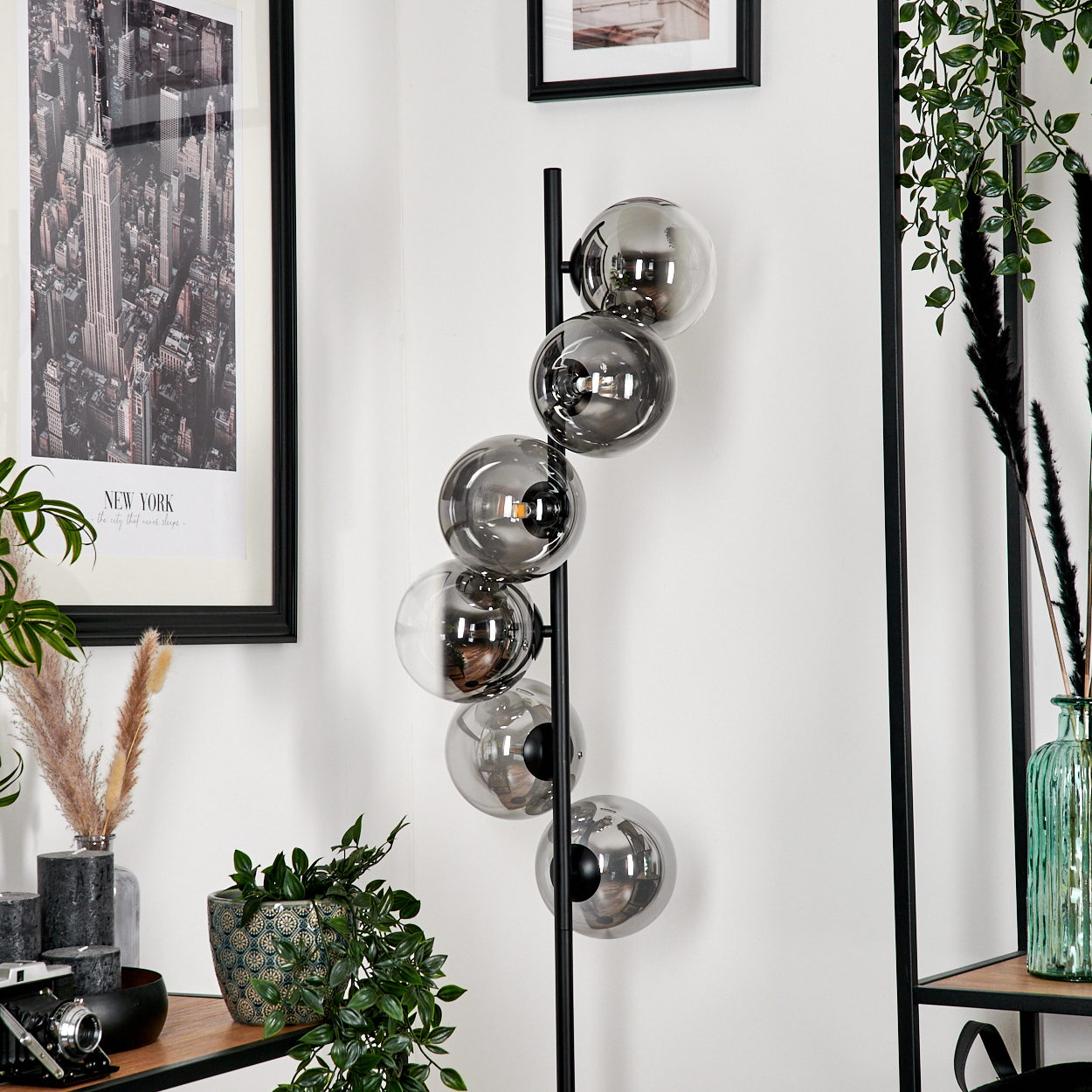 Eine Stehlampe mit mehreren Glaskugelleuchten, schwarzem Stiel und rundem Fuß, vor einer weißen Wand.