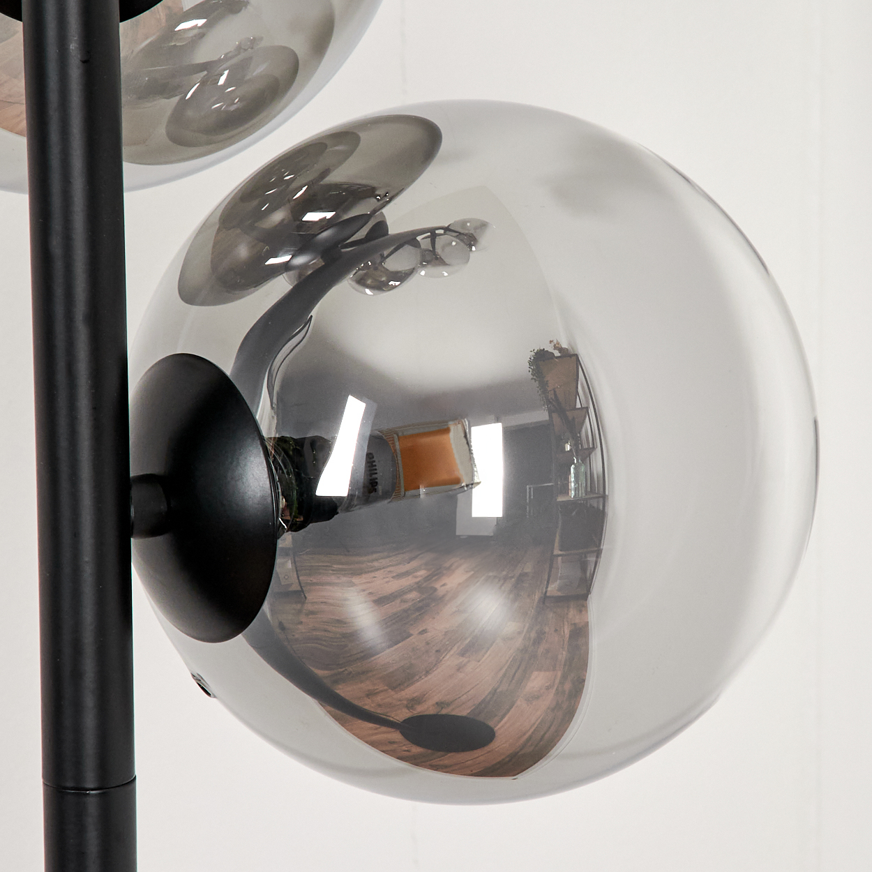 Eine Stehlampe mit schwarzem Ständer und mehreren transparenten grauen Glaskugeln, die den Raum reflektieren.
