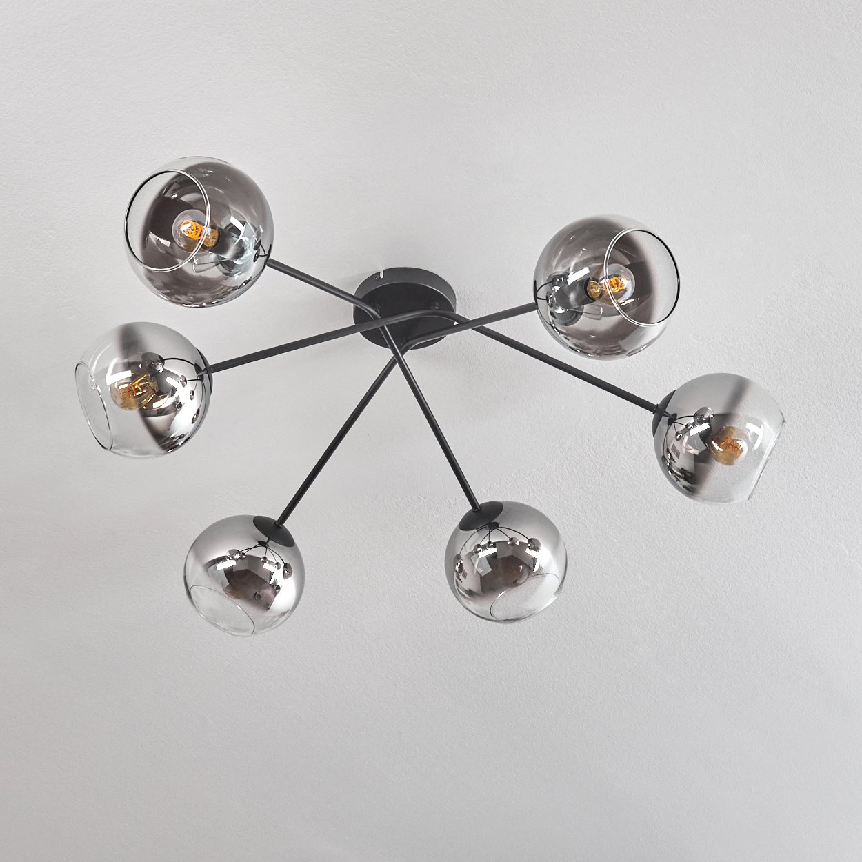 Deckenlampe mit sechs verchromten Kugeln und schwarzen Armen, von unten gesehen.