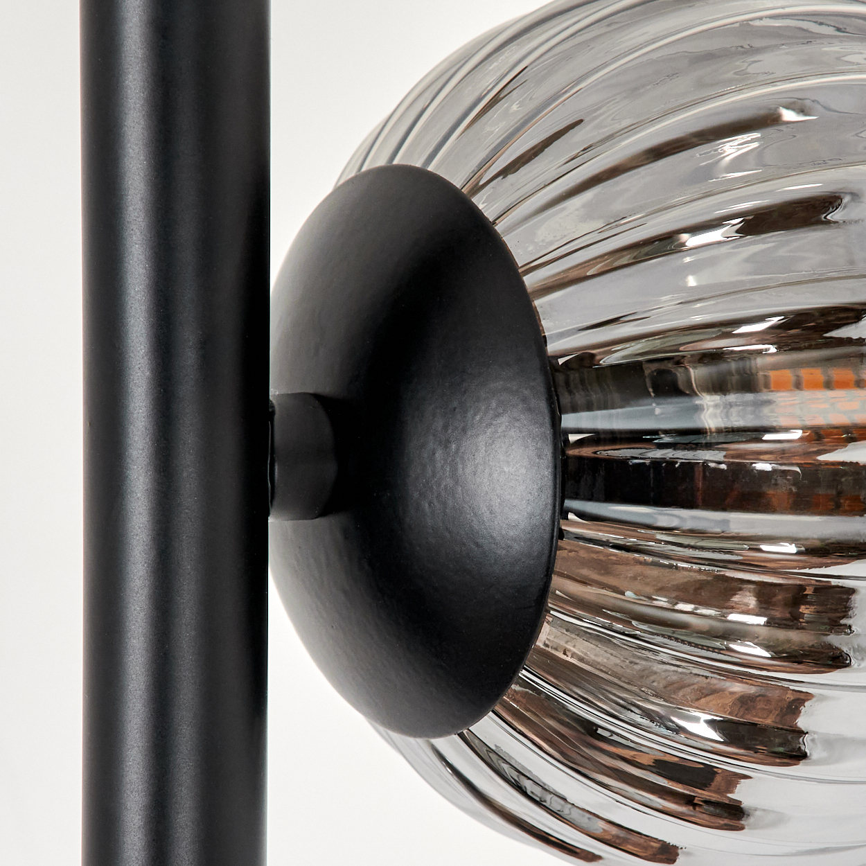 Nahaufnahme einer schwarzen Lampe mit einem gerippten, grauen Glaskugel und schwarzem Sockel.