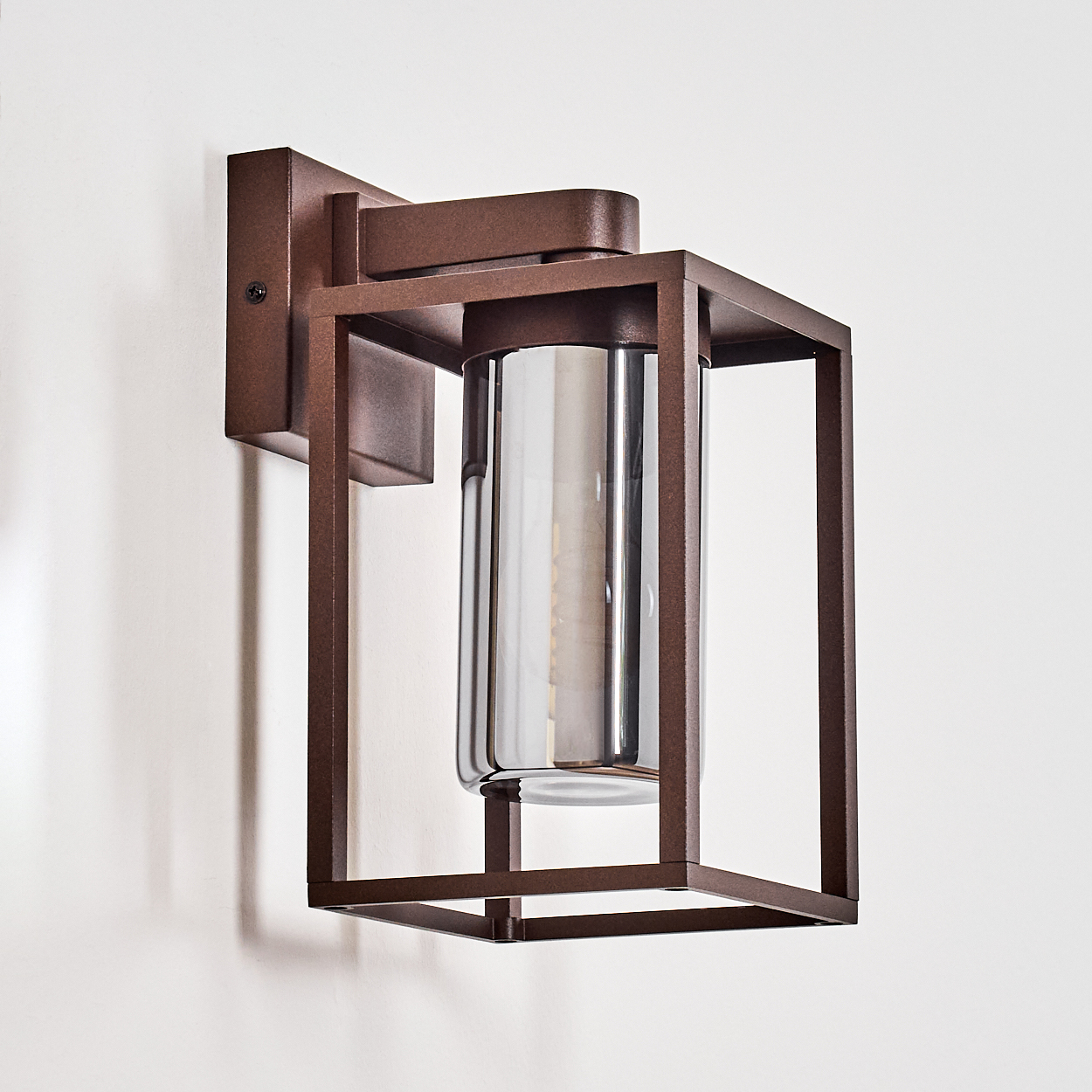 Eine bronzefarbene, quadratische Außenlampe mit einem klaren, zylindrischen Glasschirm.