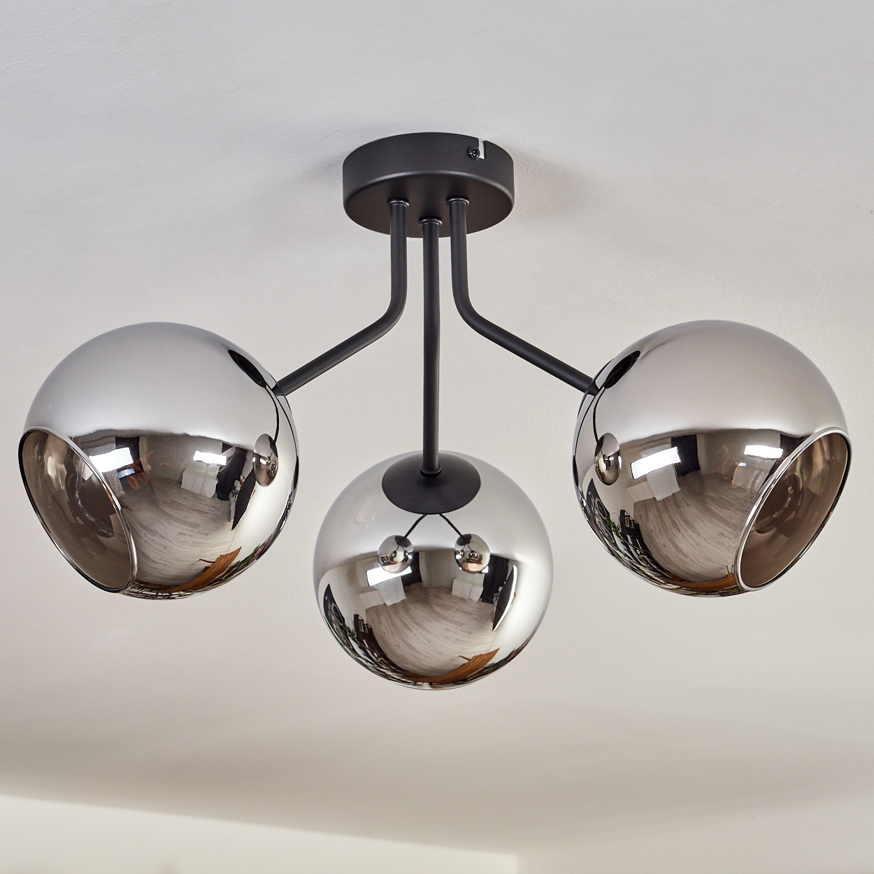 Eine Deckenlampe mit drei grauen Kugeln, die den Raum darunter reflektieren.