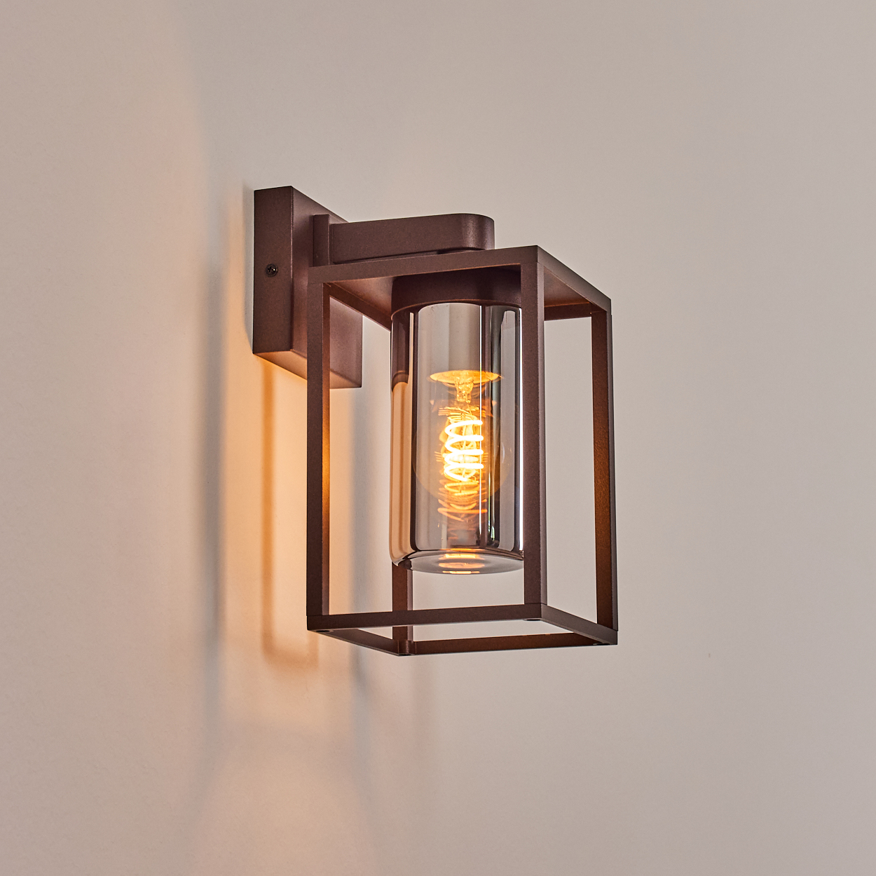 Eine braune Wandlampe mit rechteckigem Rahmen und zylindrischem Glasschirm.