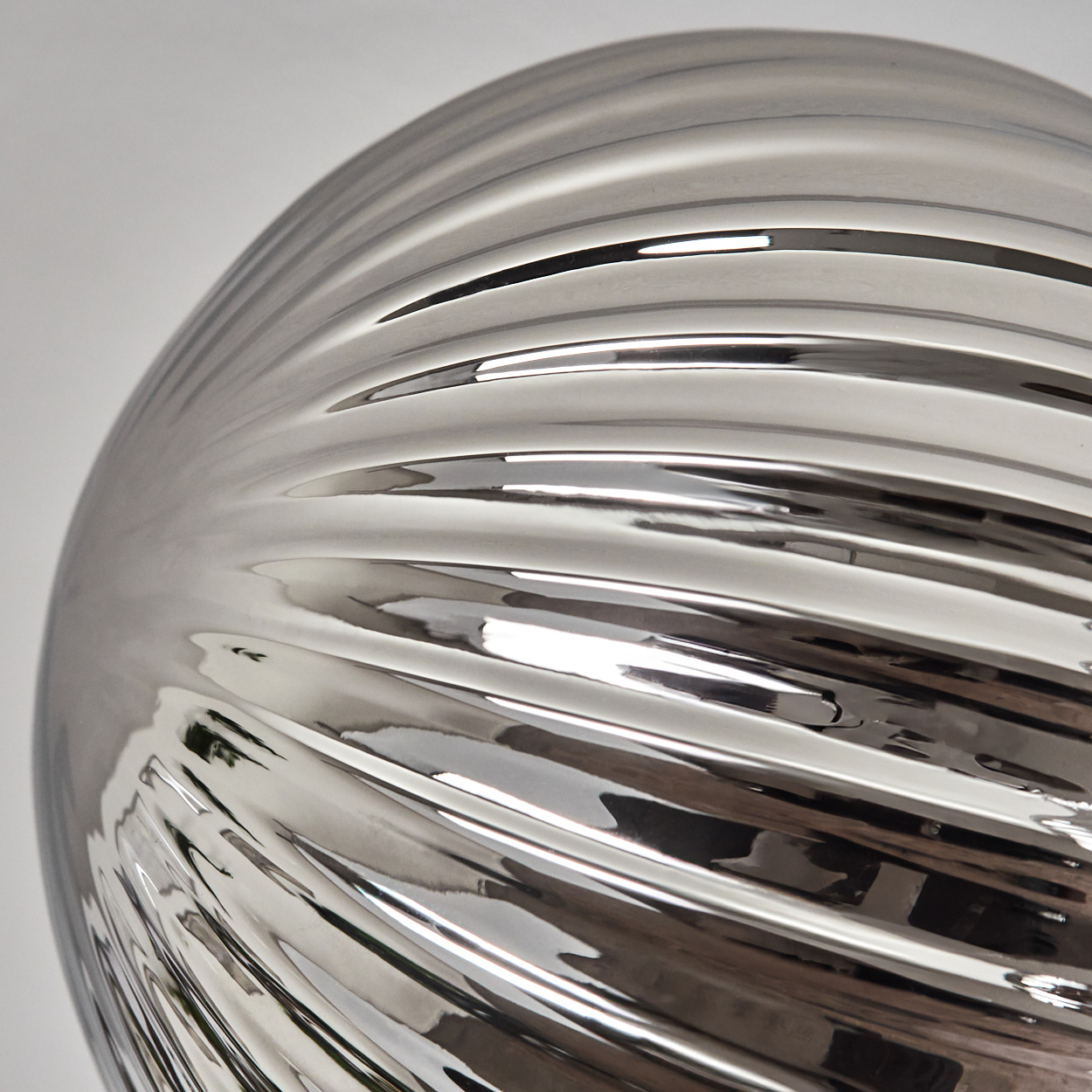 Nahaufnahme eines silbernen, geriffelten Globus. Die Oberfläche reflektiert die umgebenden Objekte.