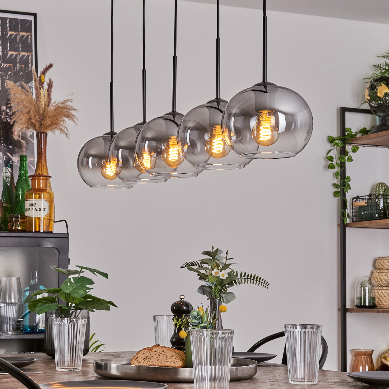 Esszimmer mit Hängelampen. Runde Glasschirme mit sichtbaren Glühbirnen. Tisch mit Gläsern und Essen gedeckt.