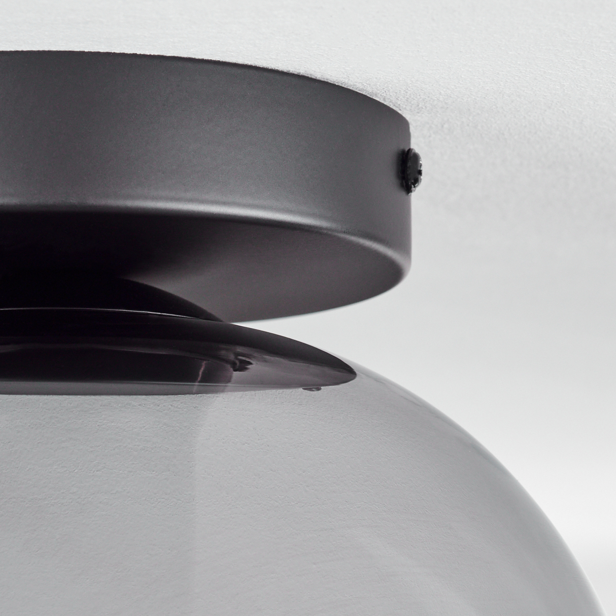 Nahaufnahme des oberen Teils einer schwarzen Lampe, darunter ein Glasschirm. Die Decke ist weiß.