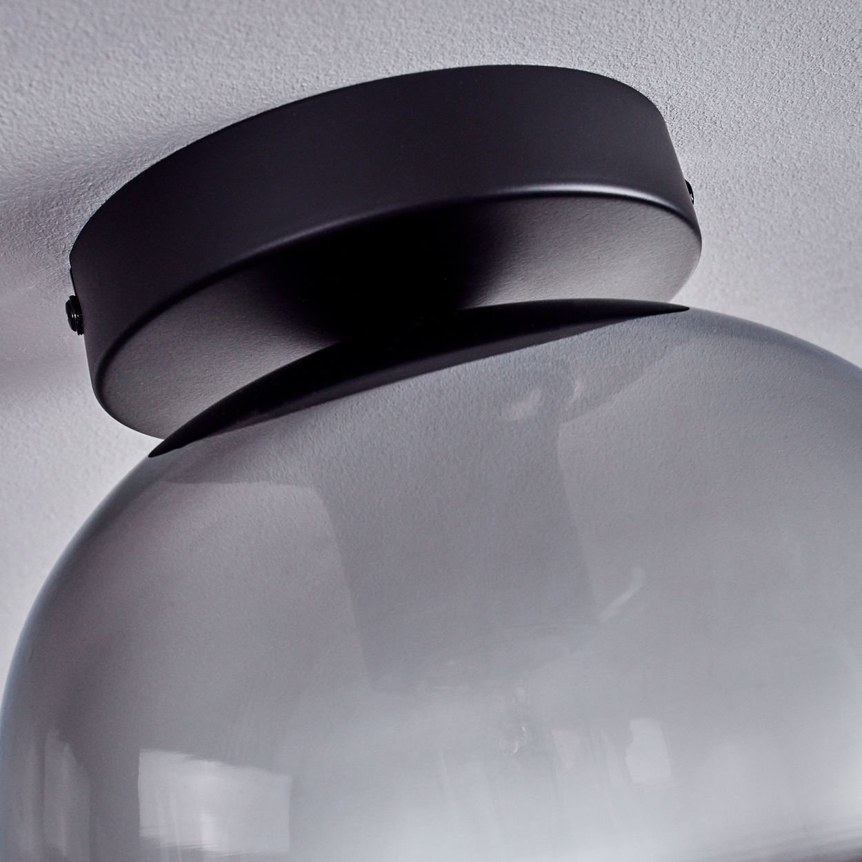 Nahaufnahme einer Deckenleuchte. Die Lampe hat einen schwarzen Sockel und einen rauchigen Glasschirm.