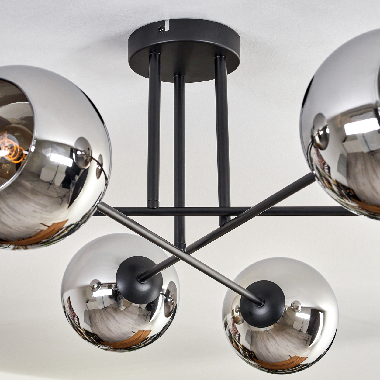 Nahaufnahme einer Deckenlampe mit sechs verspiegelten Kugelschirmen. Der schwarze Rahmen und die Glühbirnen sind sichtbar.