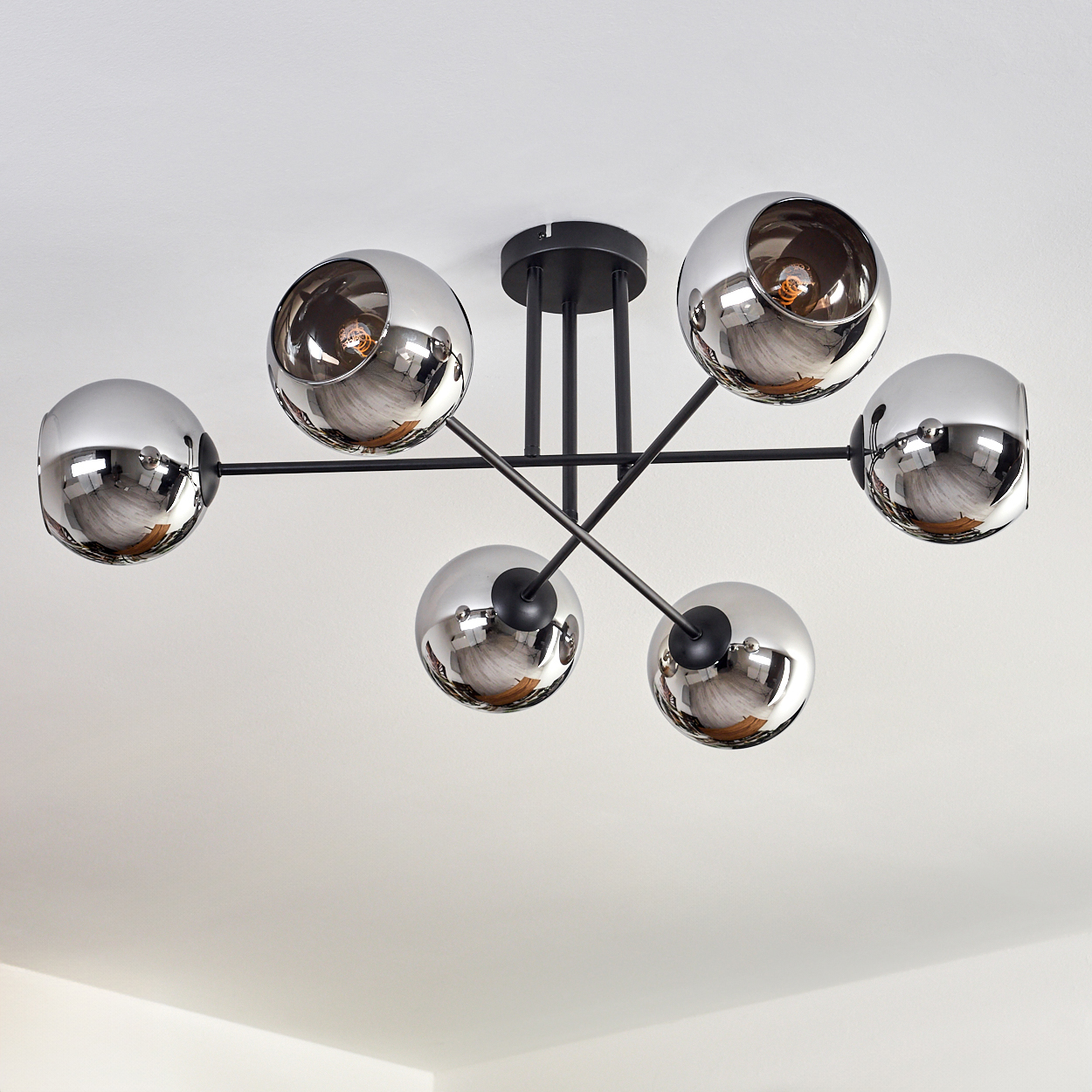 Eine Deckenlampe mit sechs verspiegelten Kugelschirmen. Der schwarze Rahmen ist sichtbar. Das Licht ist hell.