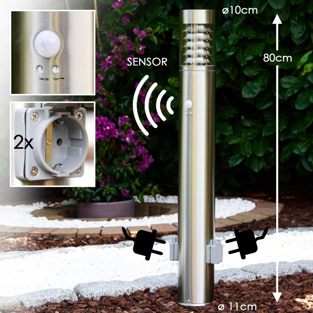 Eine Außenleuchte aus Edelstahl mit Sensor und zwei Steckdosen. Das Licht ist neben einem Garten und hat Stecker.