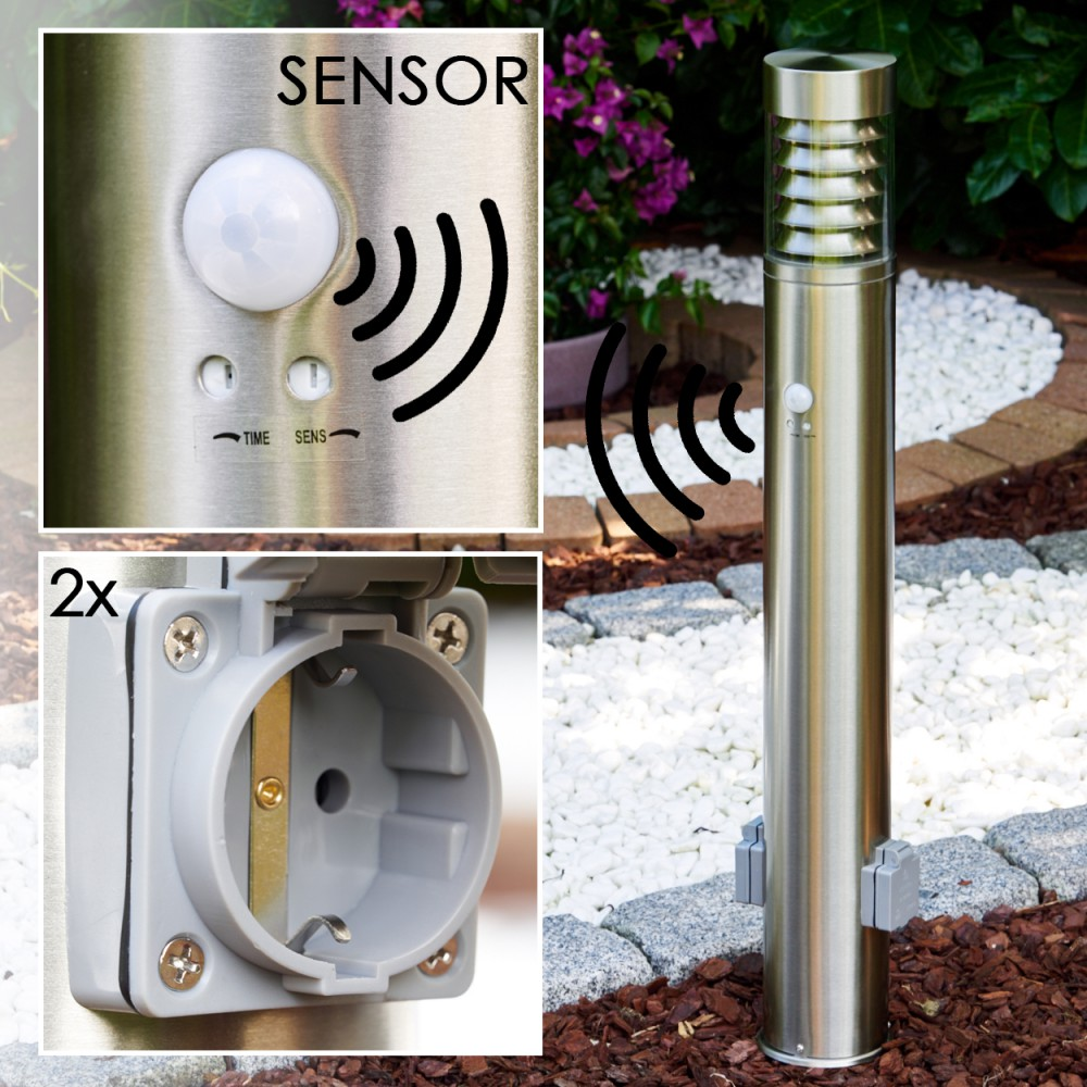 Nahaufnahme einer silbernen Außenleuchte mit Sensor. Die Leuchte hat auch eine Steckdose und einen Garten im Hintergrund.