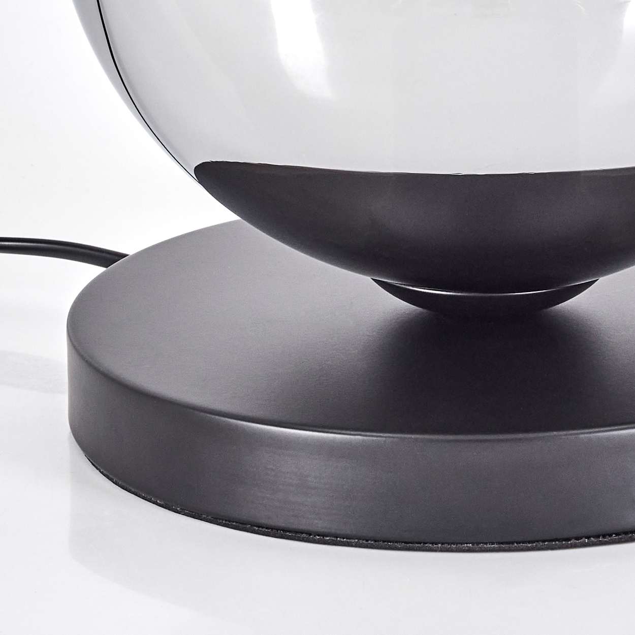 Nahaufnahme einer Lampe mit schwarzem Sockel und Glaskugel. Die Glühbirne befindet sich in der Kugel. Weißer Hintergrund.
