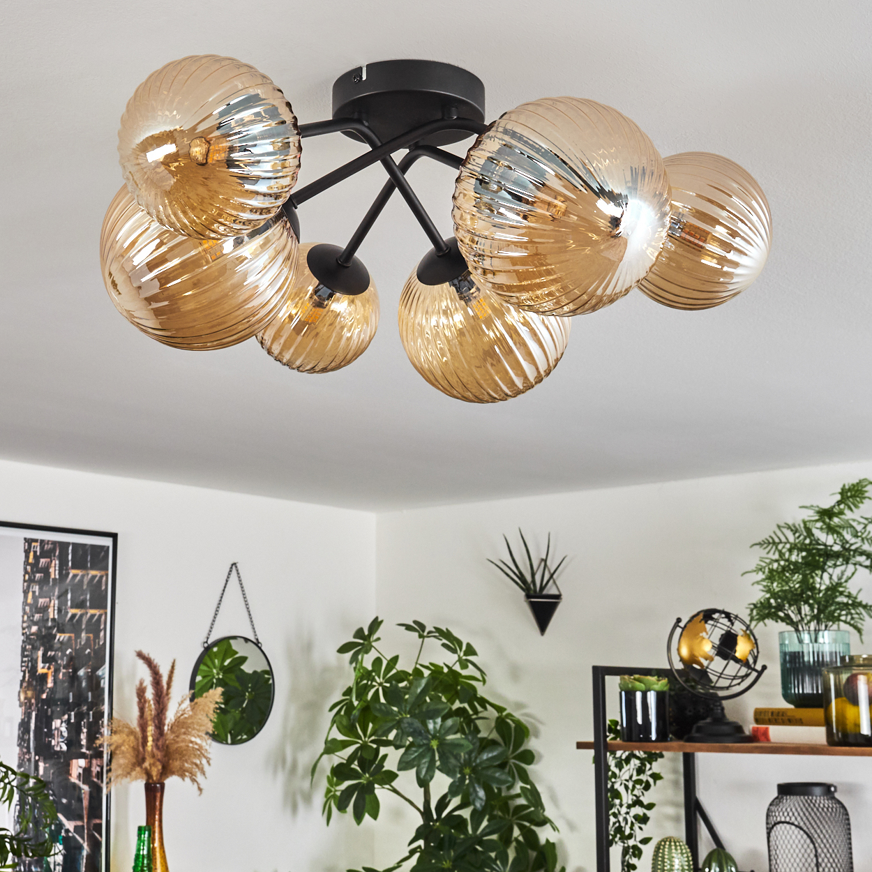 Eine Deckenlampe mit sieben bernsteinfarbenen Glaskugeln, schwarzen Armen und einem schwarzen Sockel, in häuslicher Umgebung.