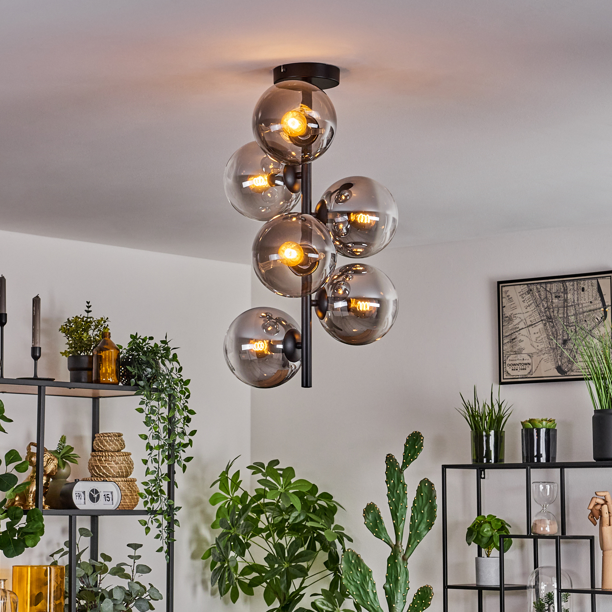 Deckenlampe mit rauchfarbenen Glaskugeln. Raum mit Pflanzen und Deko im Hintergrund. Glühbirnen leuchten.