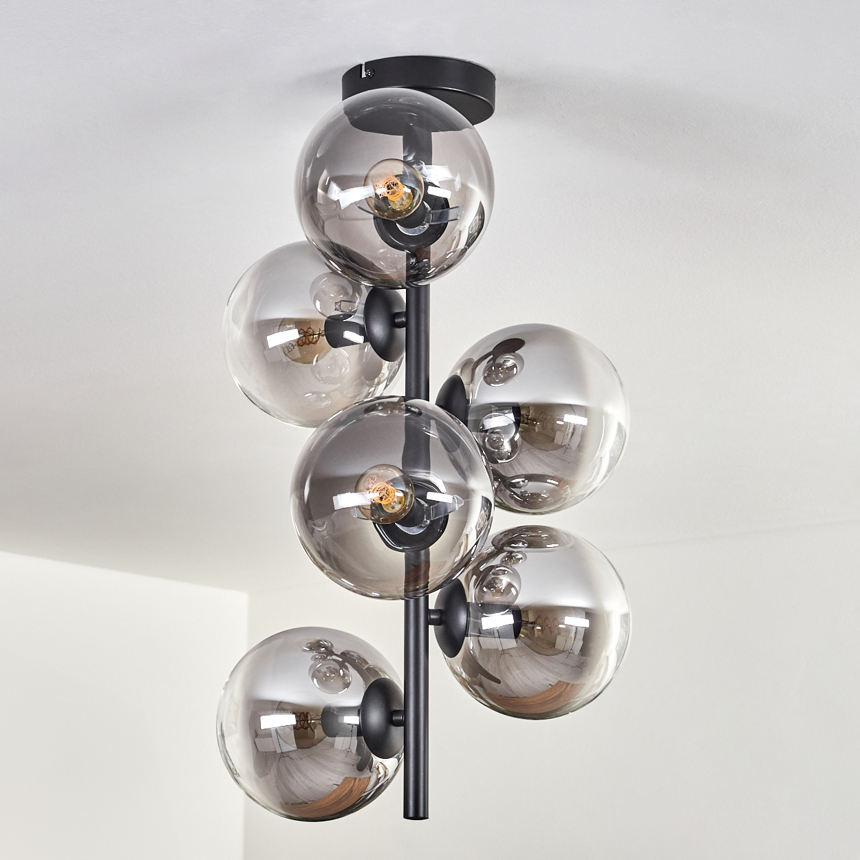 Deckenlampe mit mehreren rauchfarbenen Glaskugeln, jede mit sichtbarer Glühbirne. Raum mit Pflanzen und Deko.