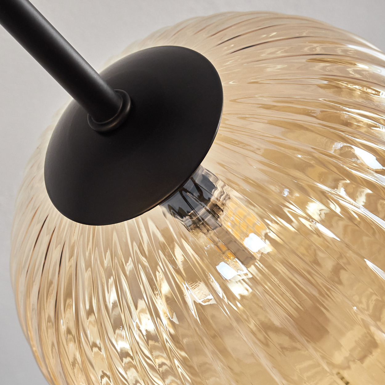 Nahaufnahme einer Glühbirne in einer goldenen, geriffelten Glaskugel. Die Glühbirne leuchtet, mit schwarzem Halter.