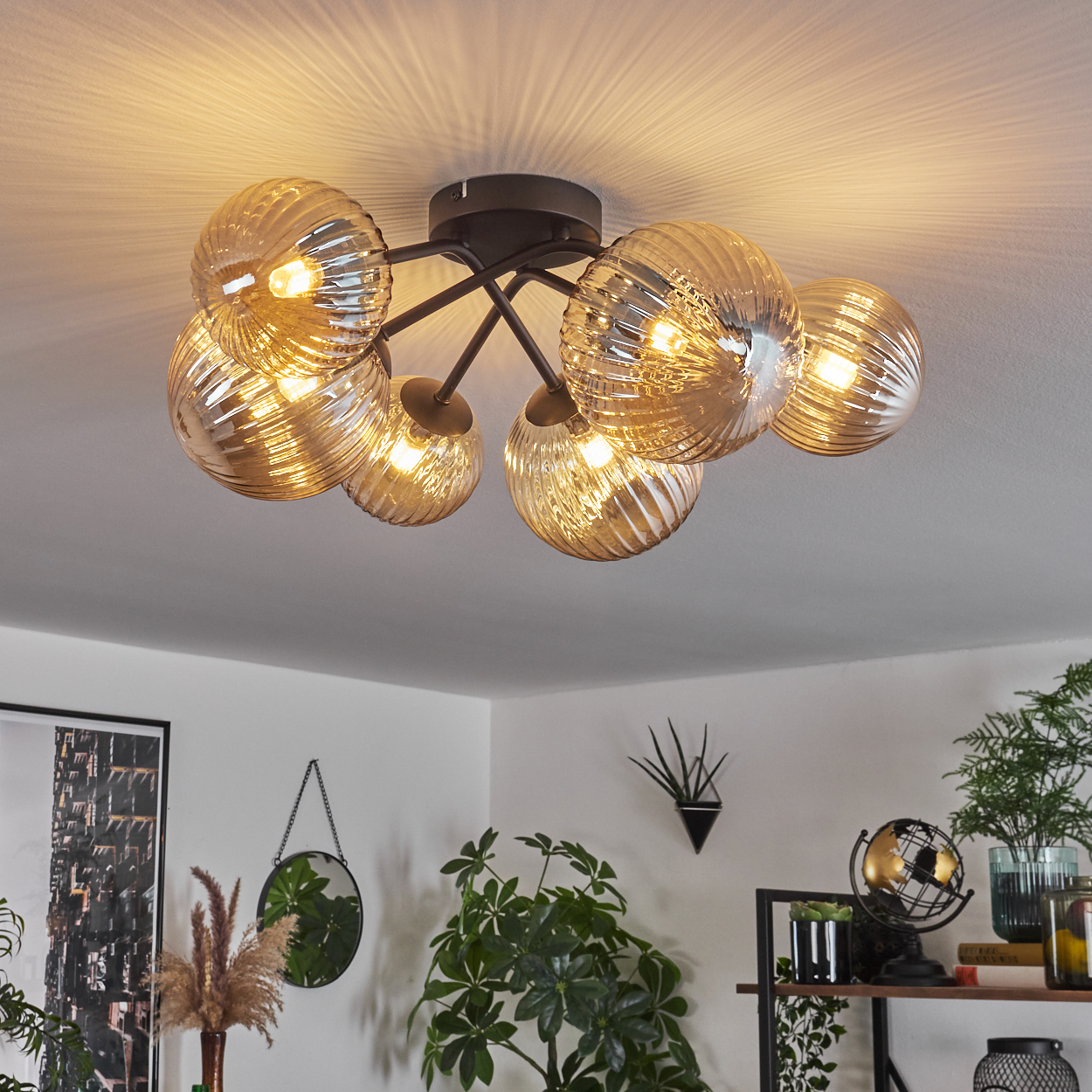 Deckenlampe mit goldenen, geriffelten Glaskugeln. Glühbirnen leuchten. Die Lampe befindet sich in einem Raum.