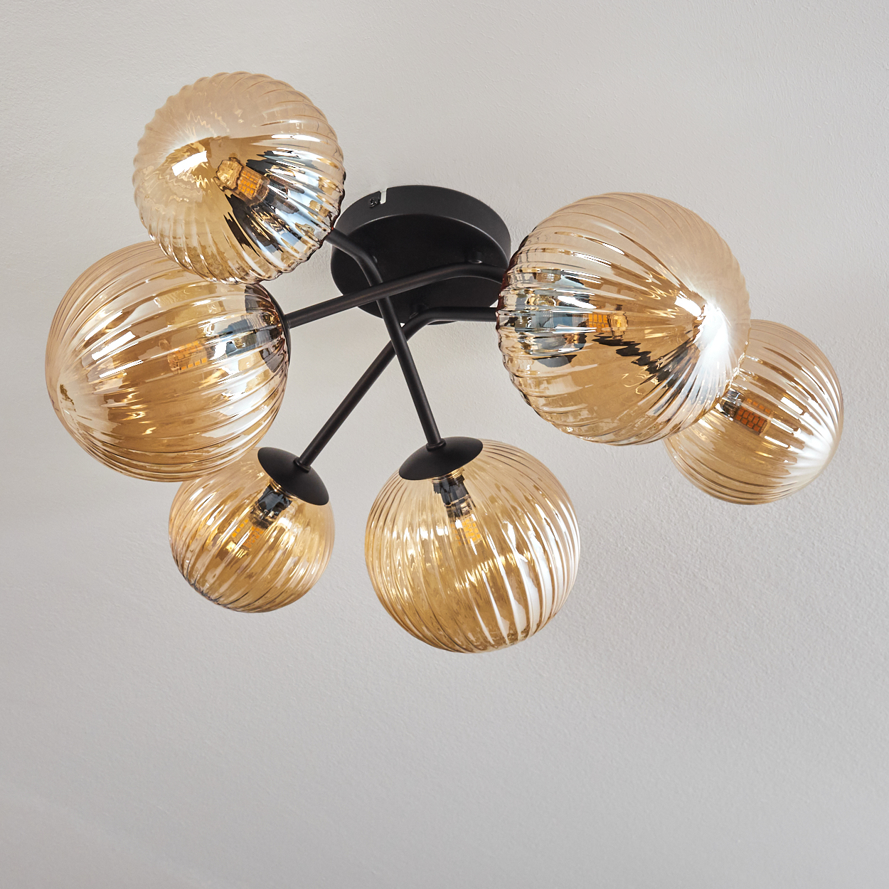Deckenlampe mit goldenen, geriffelten Glaskugeln. Die Lampe befindet sich in einem Raum, die Lichter sind an.