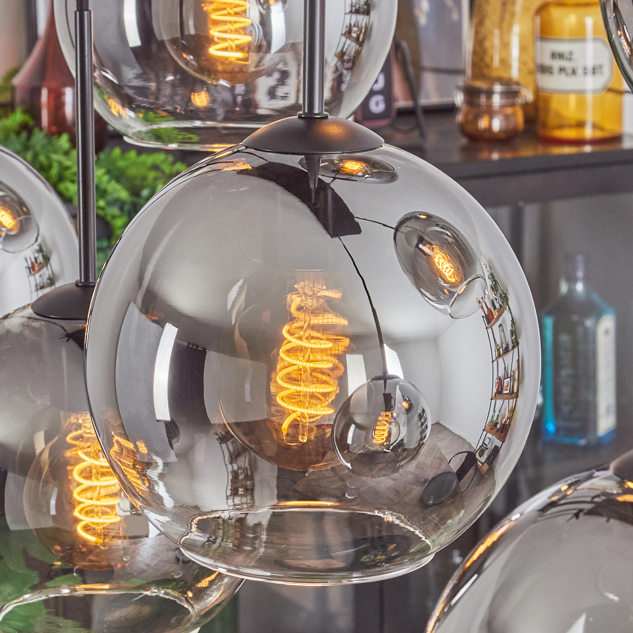 Nahaufnahme eines Clusters von kugelförmigen Lampen mit sichtbaren Wendelglühbirnen und reflektierender Oberfläche.