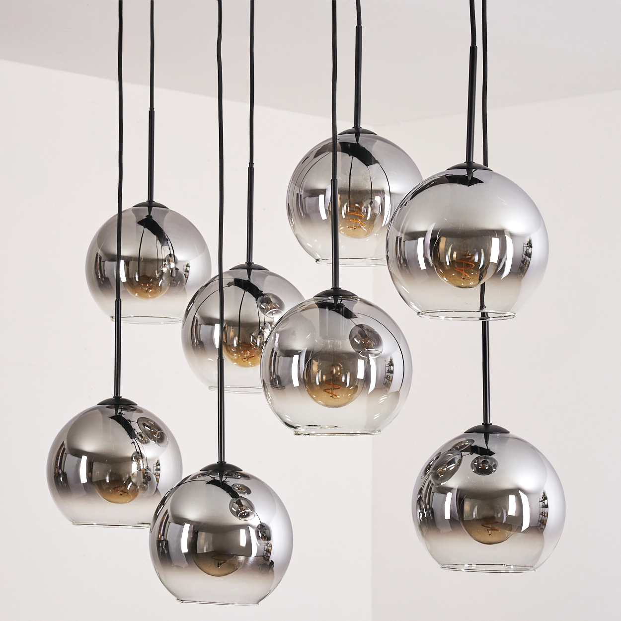 Mehrere hängende Kugellampen mit reflektierender Oberfläche und sichtbaren Glühbirnen, vor weißem Hintergrund.
