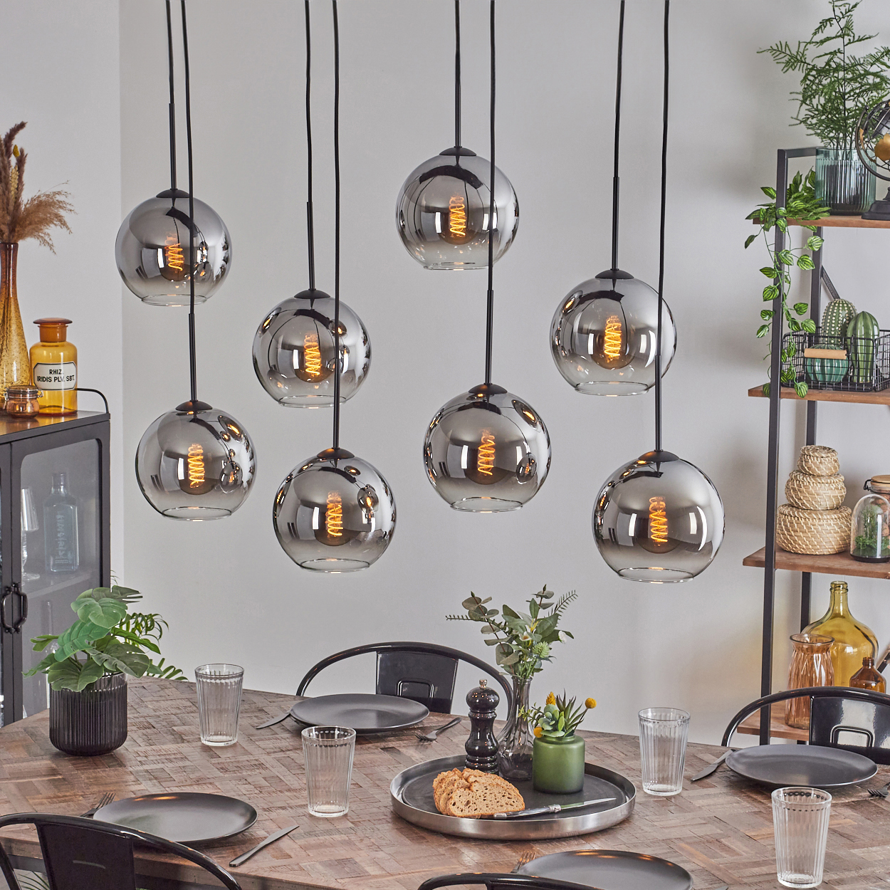 Esszimmer mit Holztisch, Gläsern, schwarzen Tellern und hängenden Leuchten mit Glaskugeln.