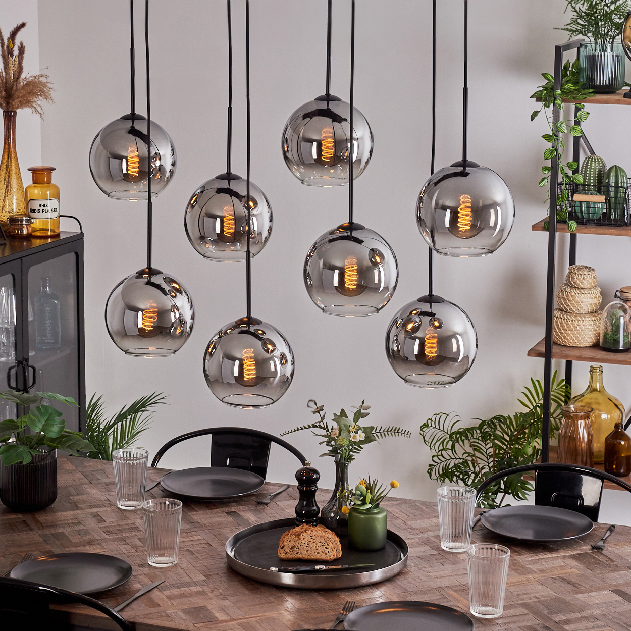 Esszimmer mit acht Pendelleuchten mit Glaskugelschirmen über einem Holztisch, gedeckt für das Abendessen.