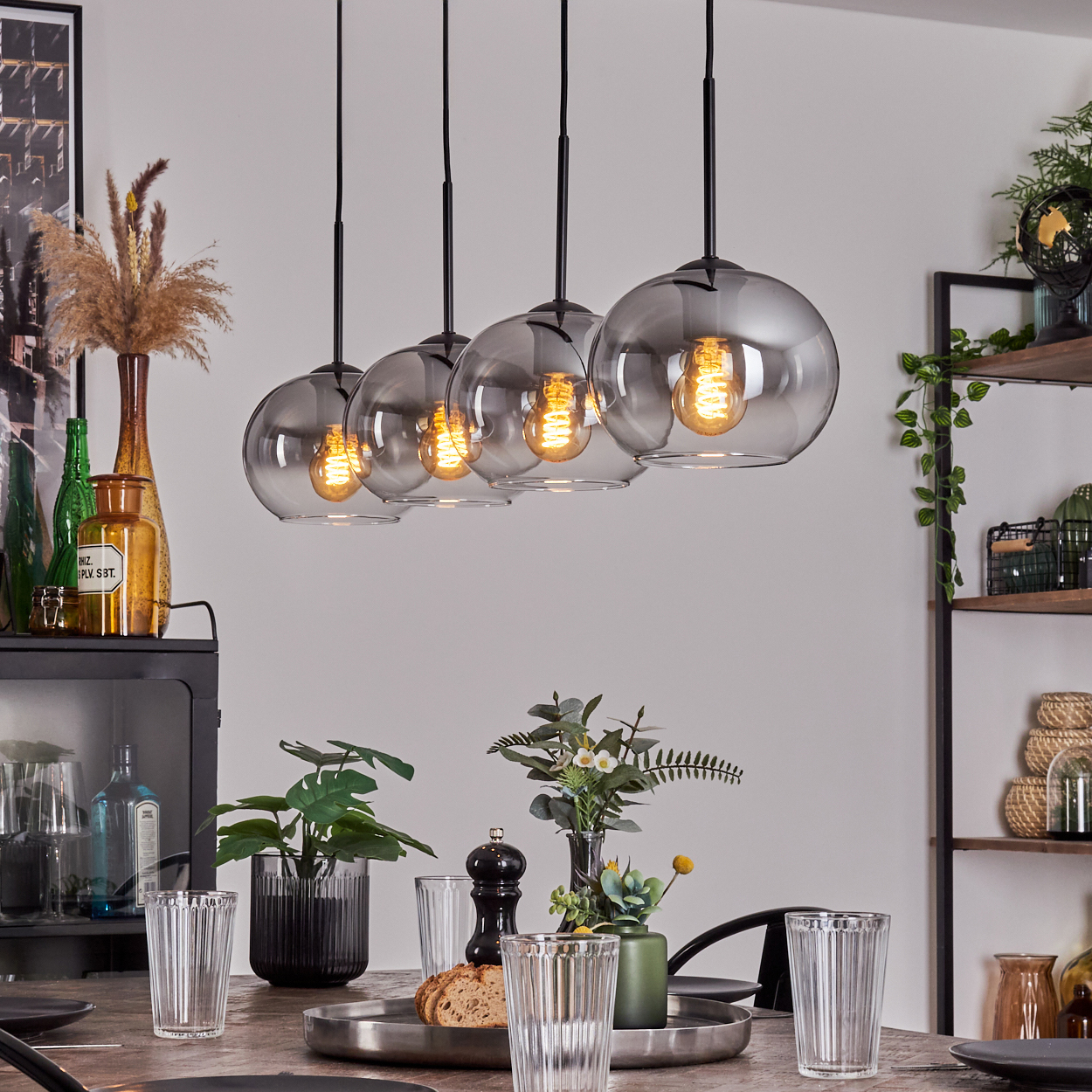 Fünf Pendelleuchten mit kugelförmigen Glasschirmen hängen über einem Tisch. Die Glühbirnen sind sichtbar.