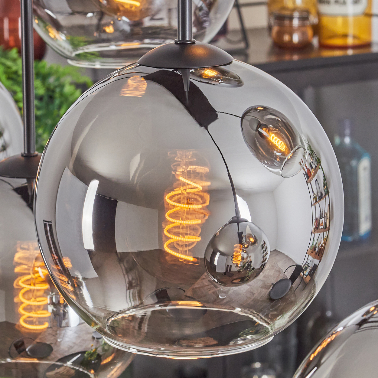 Nahaufnahme einer Glaskugel-Pendelleuchte, Glühbirne leuchtet, spiegelt die Raumdekoration.
