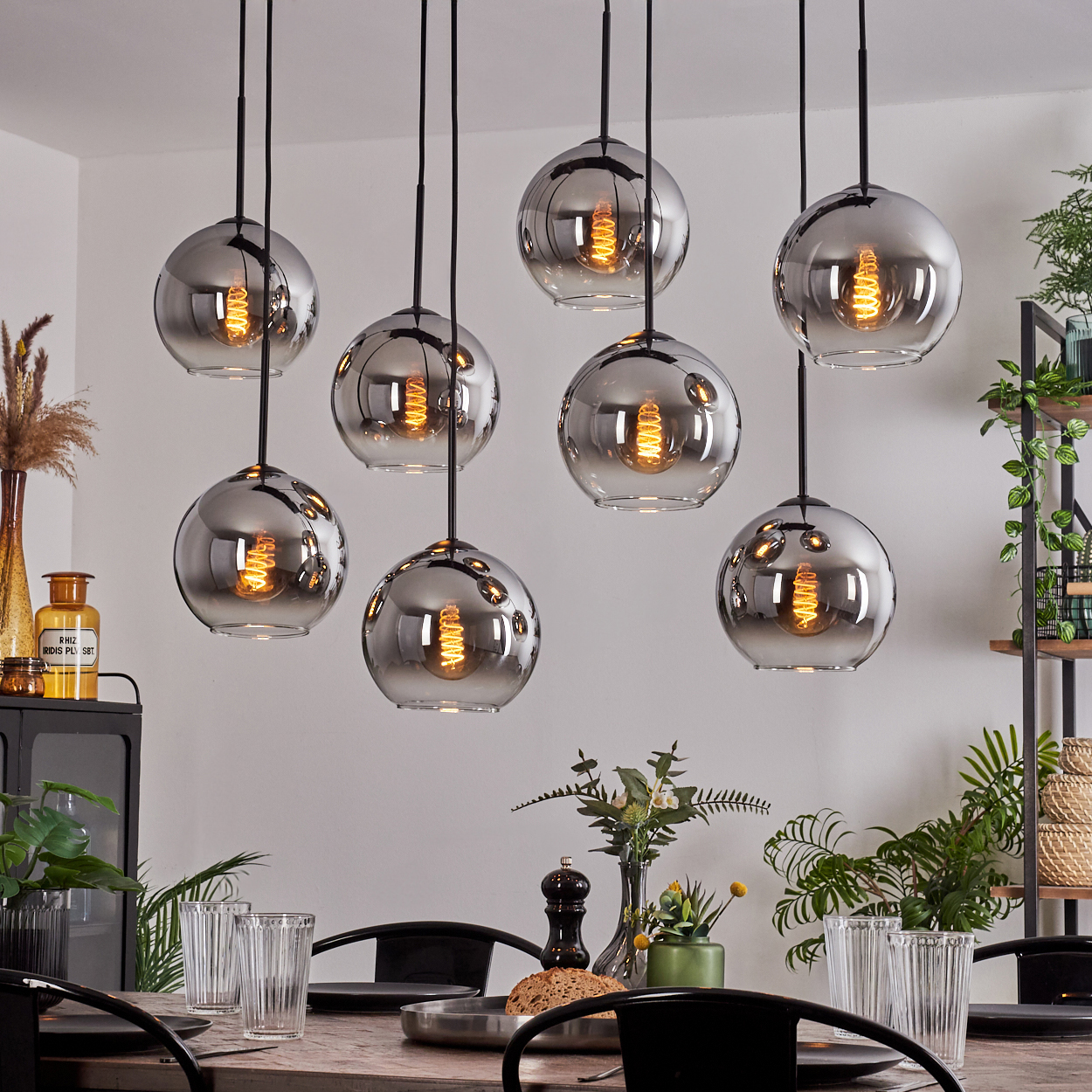 Acht Pendelleuchten mit kugelförmigen Glasschirmen hängen über einem Tisch. Die Glühbirnen sind sichtbar.