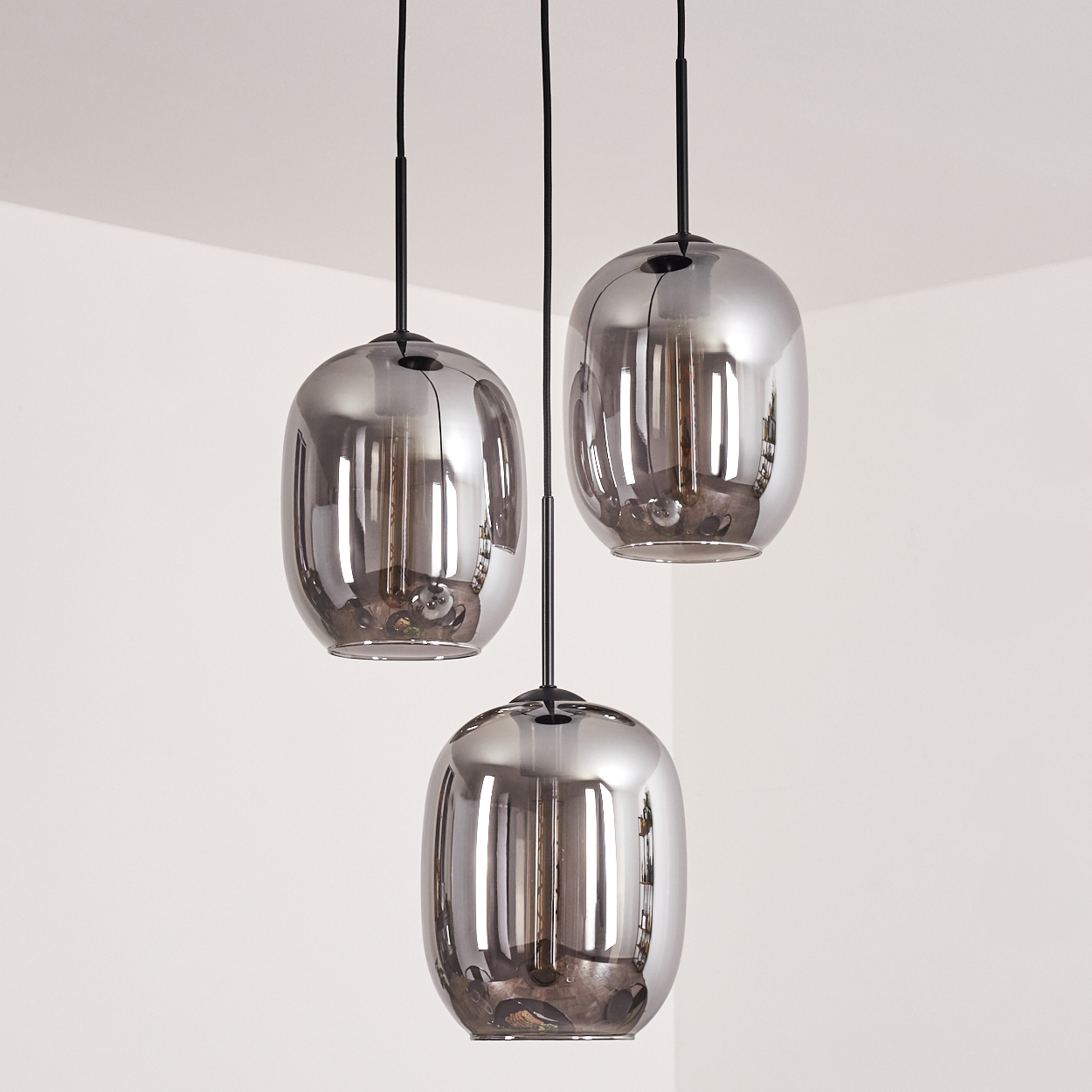 Drei Pendelleuchten mit ovalen Glasschirmen hängen von der Decke. Der Hintergrund ist eine weiße Wand.