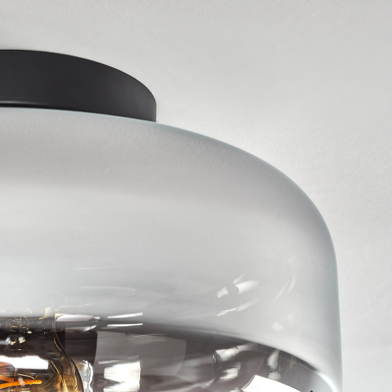 Nahaufnahme eines Lampenschirms aus Glas mit einer sichtbaren Glühbirne im Inneren. Das Glas hat einen rauchigen Gradienteneffekt.