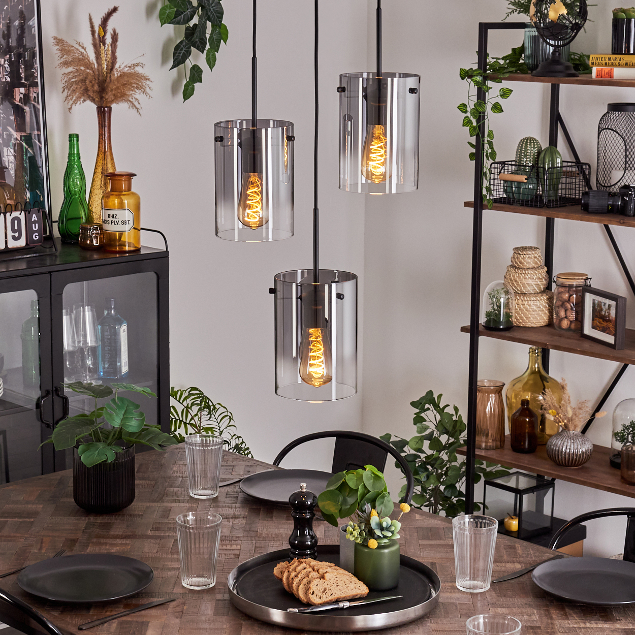 Ein Esszimmer mit drei zylinderförmigen Lampen über dem Tisch. Der Tisch ist für eine Mahlzeit gedeckt.