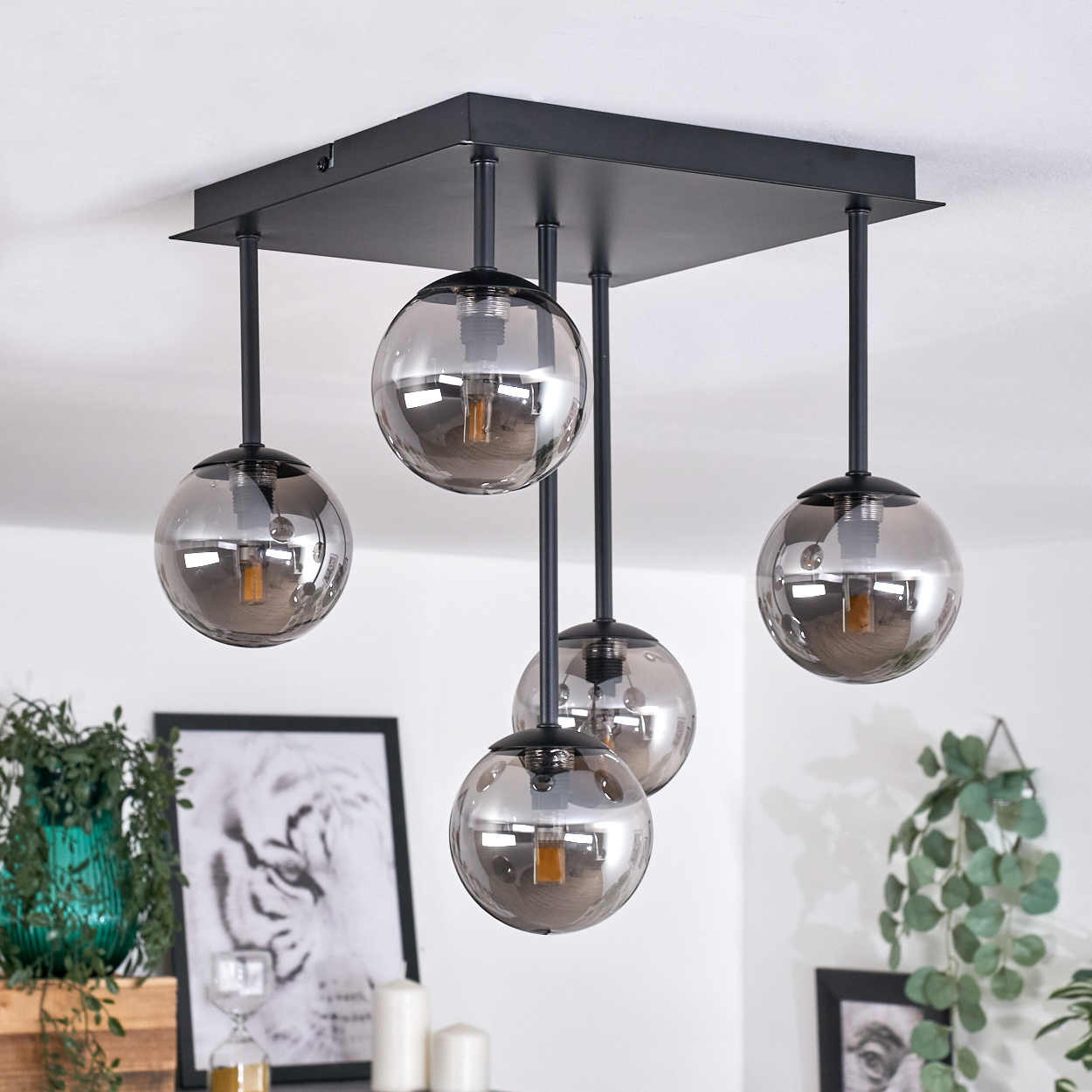 Eine Deckenlampe mit fünf silbernen Kugeln, die von einem schwarzen quadratischen Sockel hängen. Jede Kugel hat eine Glühbirne.