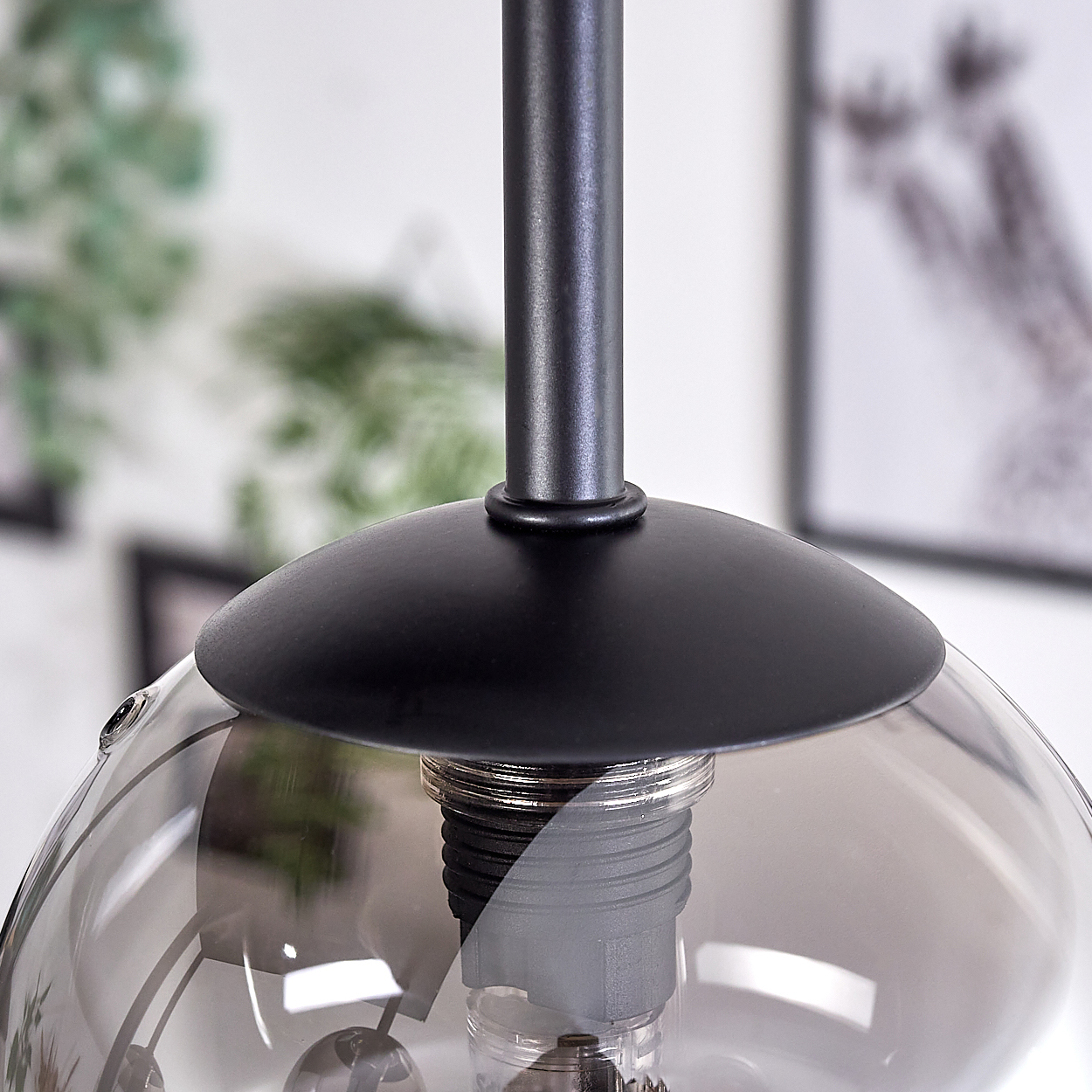 Nahaufnahme eines Glasschirms mit schwarzem Sockel. Die Glühbirne ist im transparenten Schirm sichtbar.