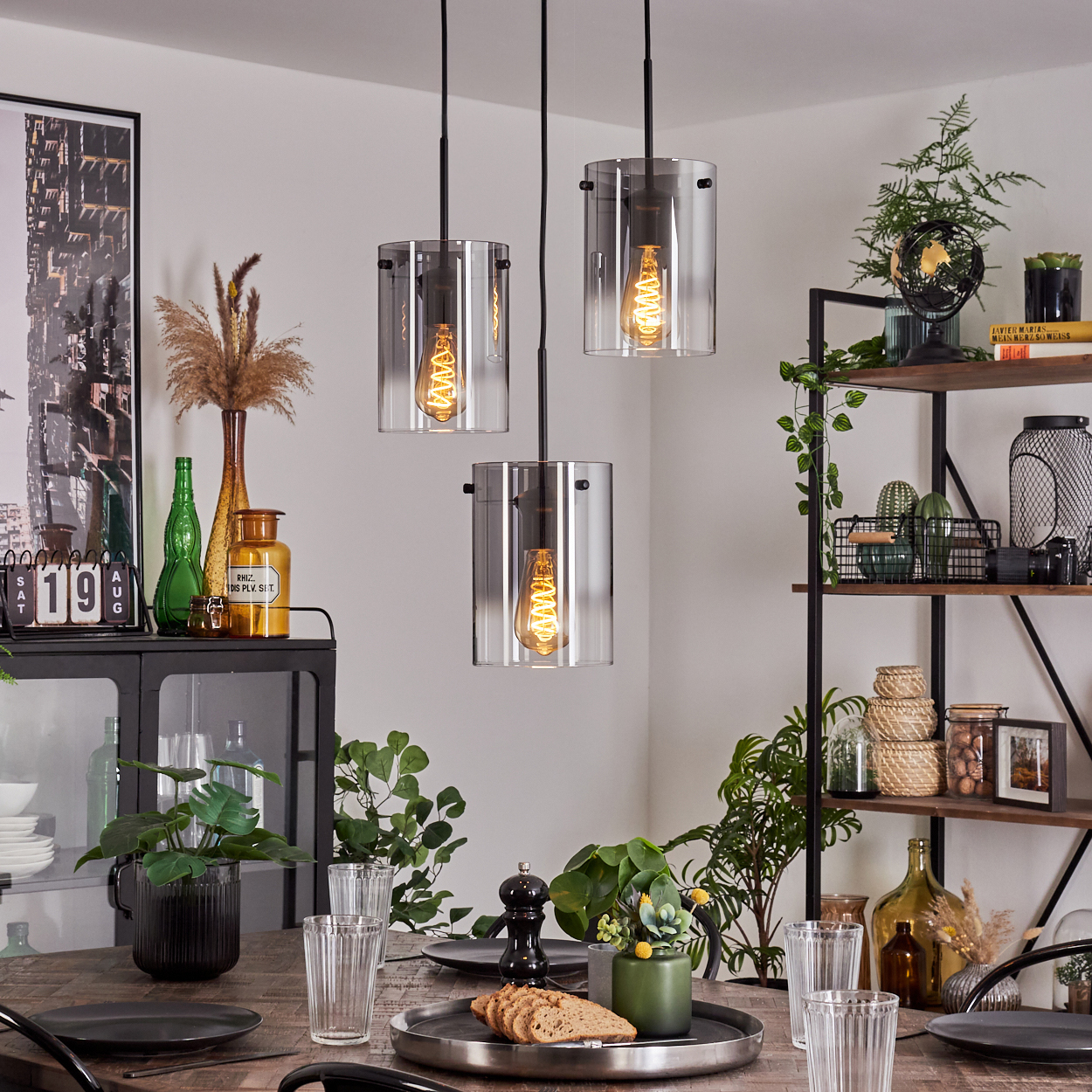 Esszimmer mit Holztisch und drei Pendelleuchten mit Glaszylindern und Spiralglühbirnen.