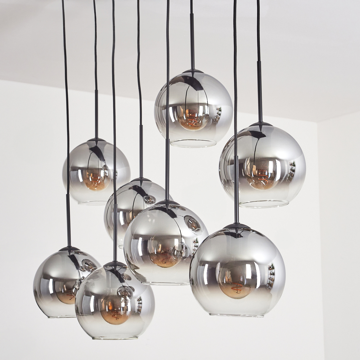 Acht Pendelleuchten mit verspiegelten Kugeln hängen von der Decke, mit sichtbaren Glühbirnen in jeder.