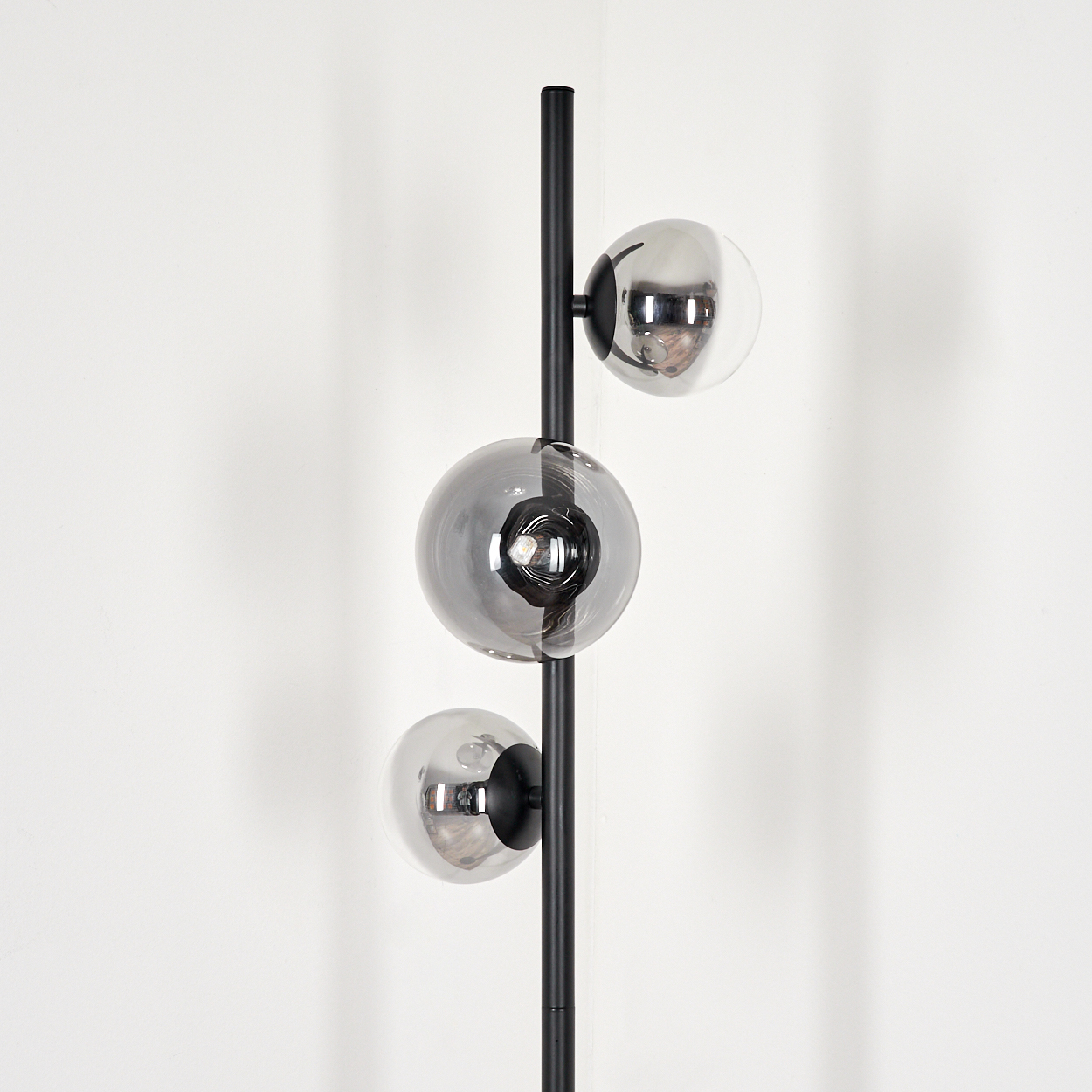 Nahaufnahme einer Stehlampe mit drei runden Glasschirmen. Die Lampe steht vor einer weißen Wand.
