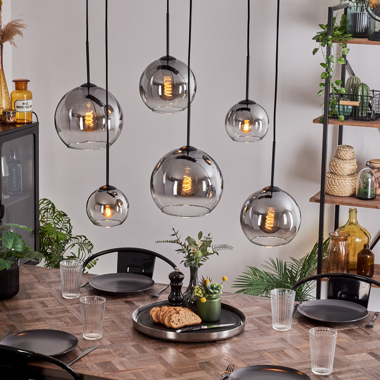 Esszimmer mit Holztisch, sechs Pendelleuchten mit Glaskugeln. Teller, Gläser und Essen sind sichtbar.