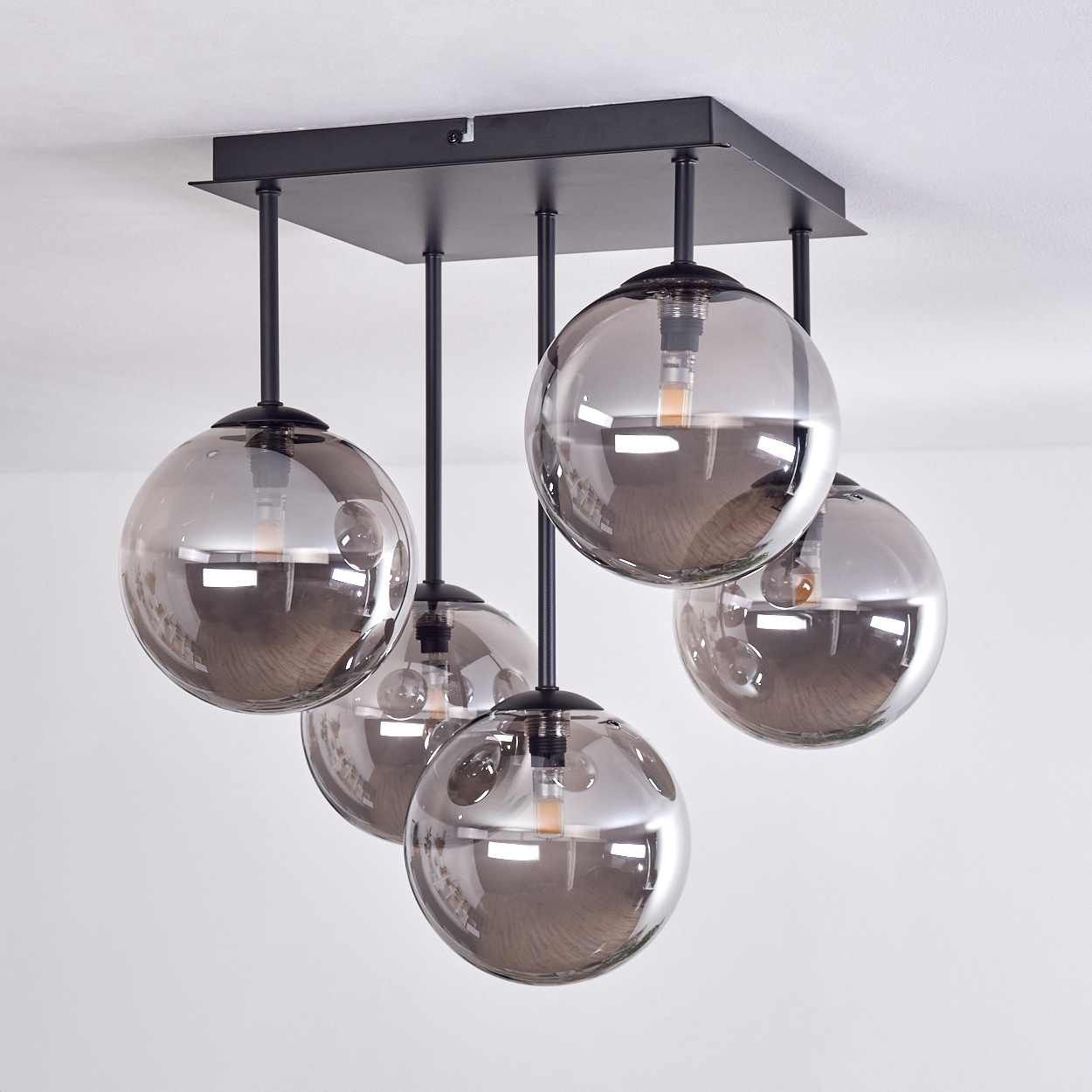Fünf Pendelleuchten mit Glasschirmen hängen von einer Decke. Sie sind kugelförmig und schwarz.